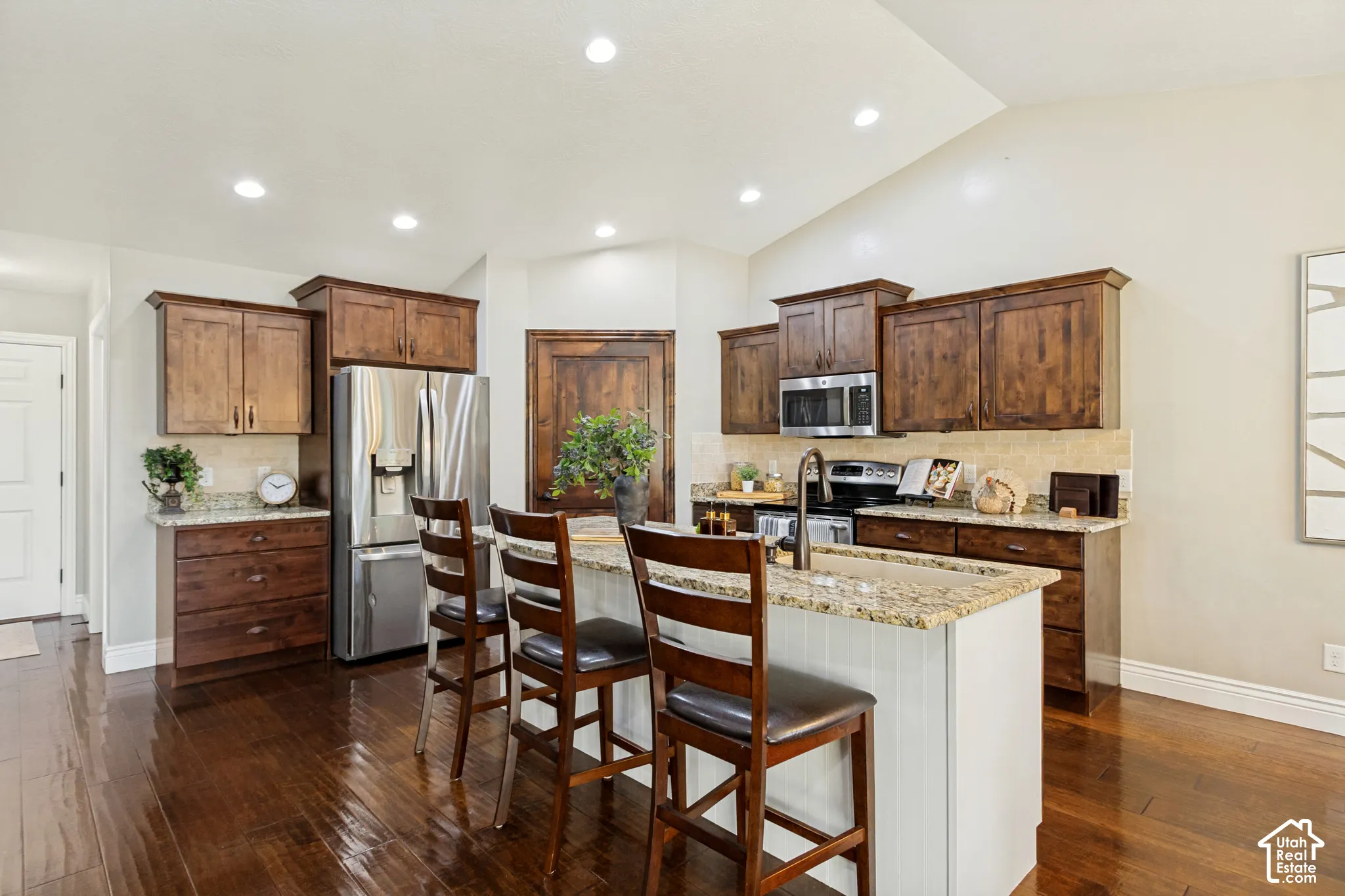 Kitchen featuring dark wood cabinetry, granite countertops, stainless steel appliances, a center island with sink, and hardwood flooring