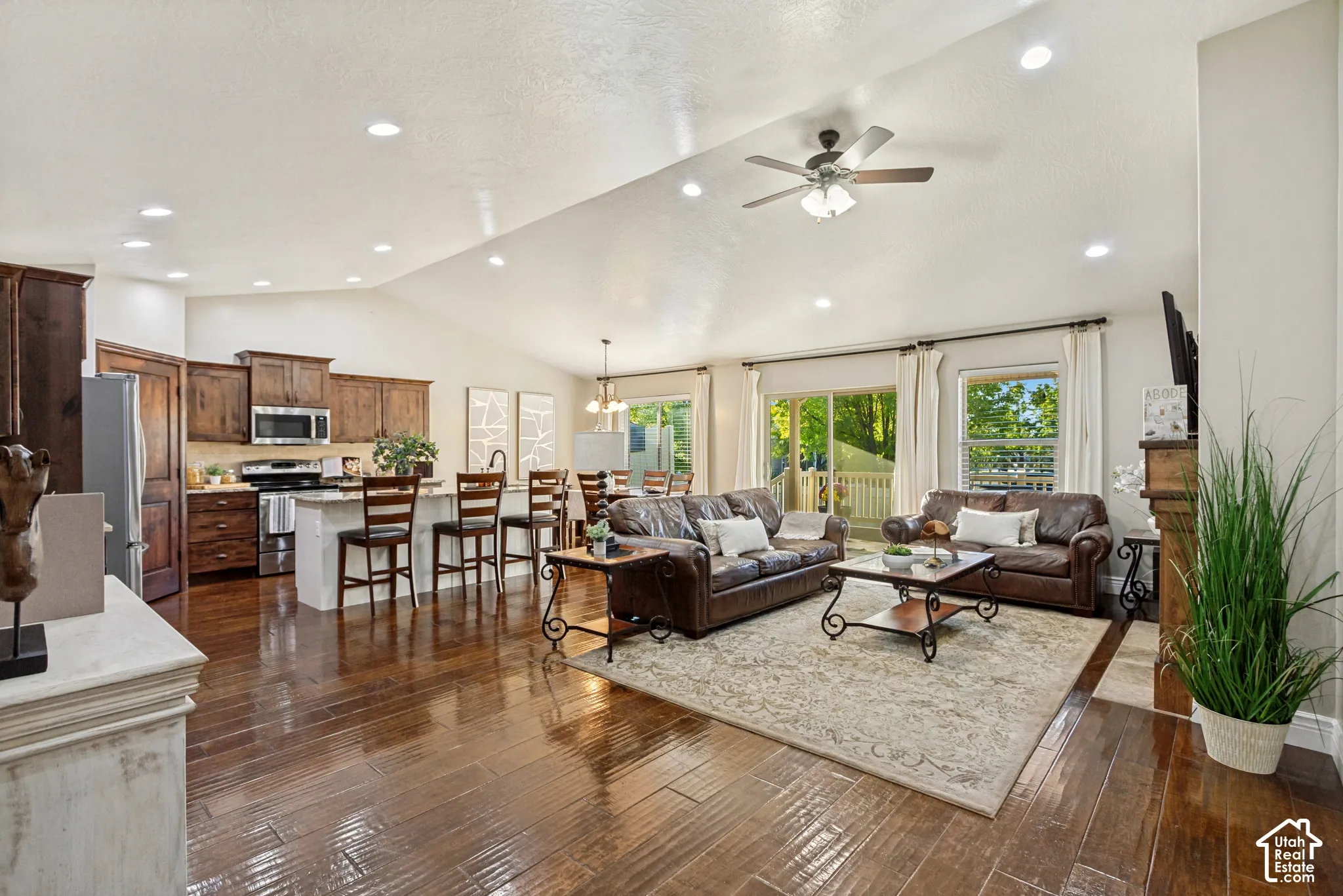 Vaulted ceilings, hardwood flooring, recessed lighting, kitchen featuring dark wood cabinetry and a central island, and a fireplace with a wood mantel