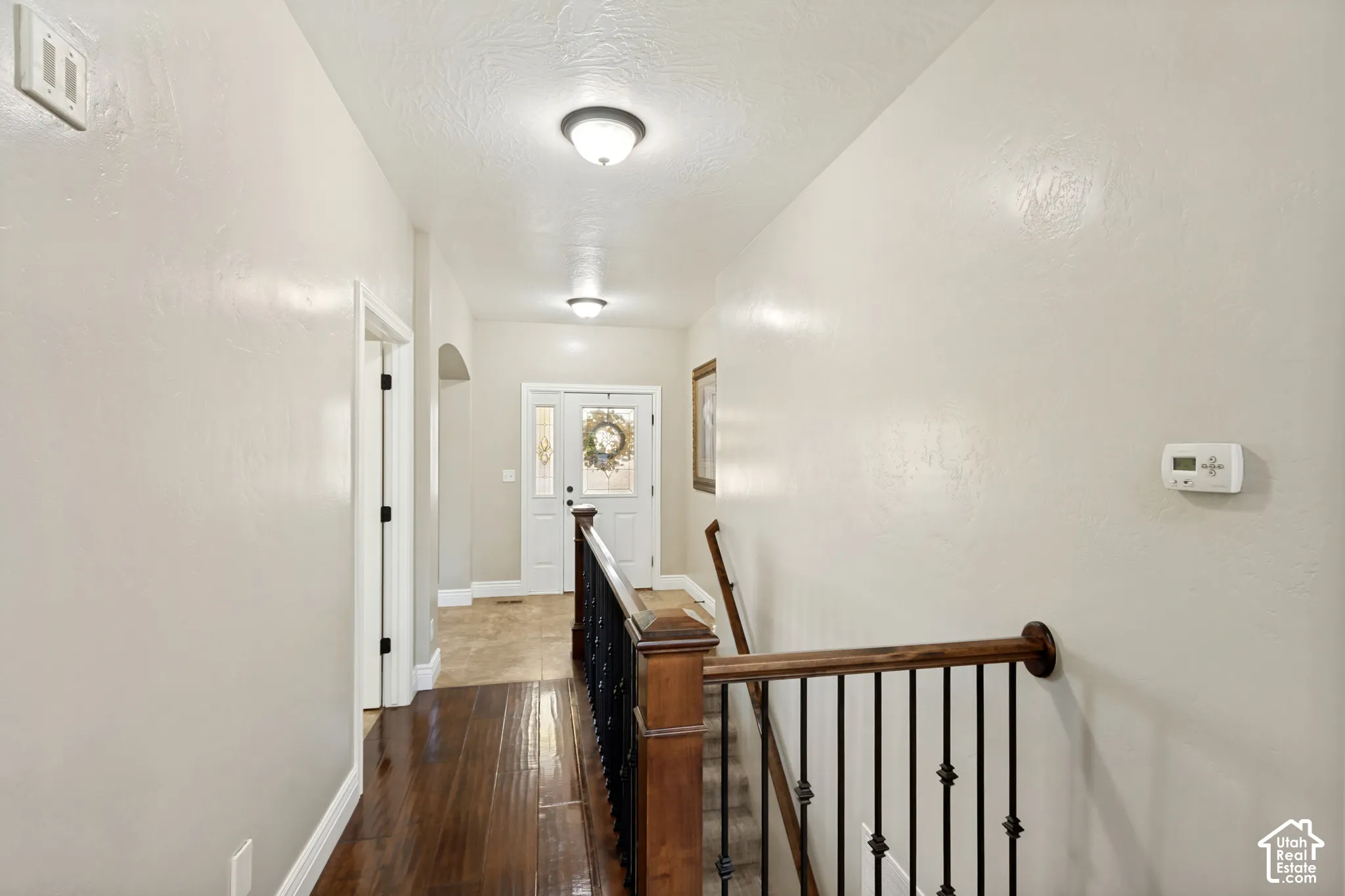 Staircase featuring dark-stained wood railings with wrought iron balusters, wood-finish flooring, neutral wall finish, and dual flush-mount ceiling light fixtures