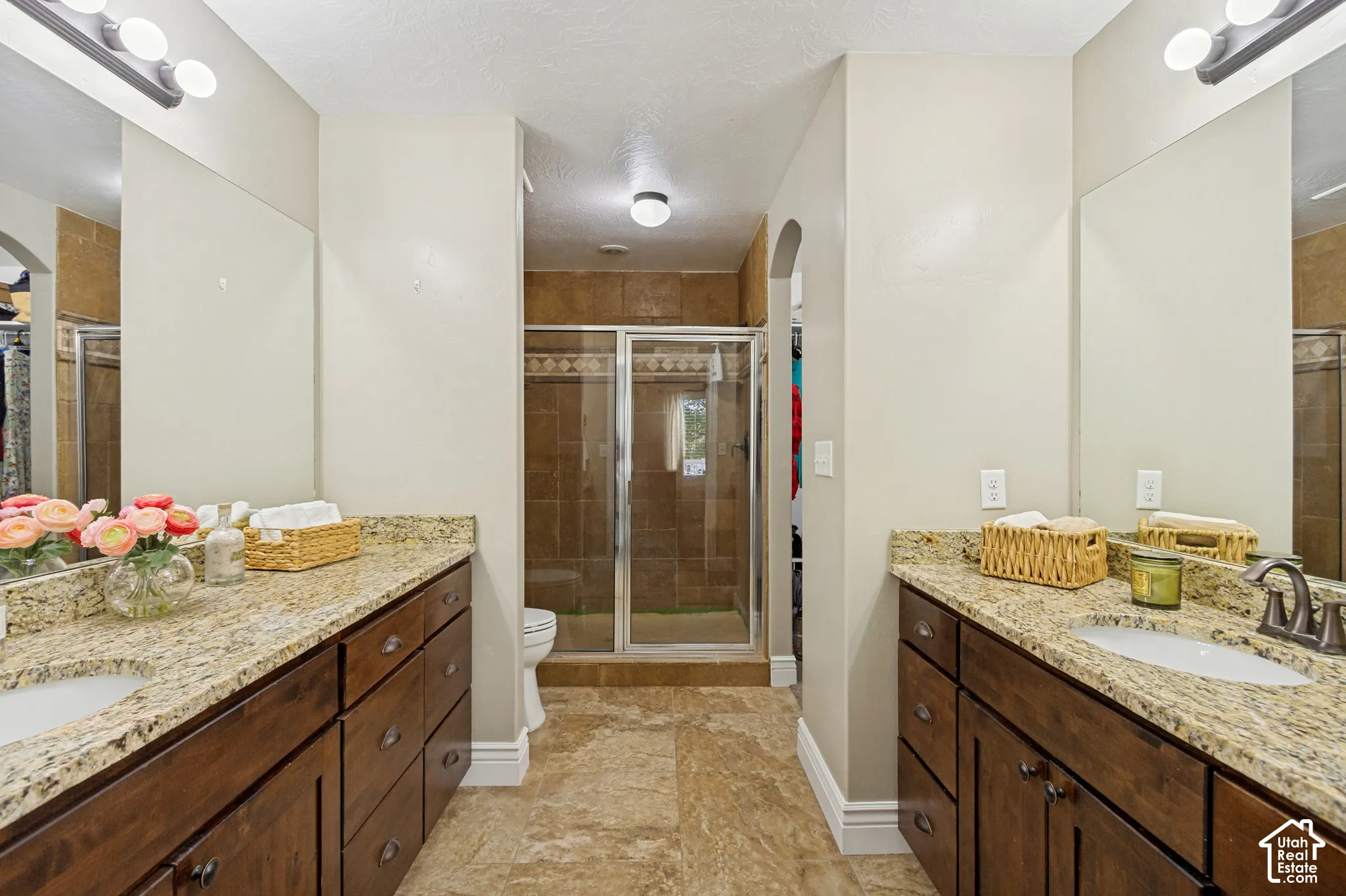 Dual vanities featuring granite countertops, dark wood-finish cabinetry, tile-surround shower with metal frame, and large wall-mounted mirrors