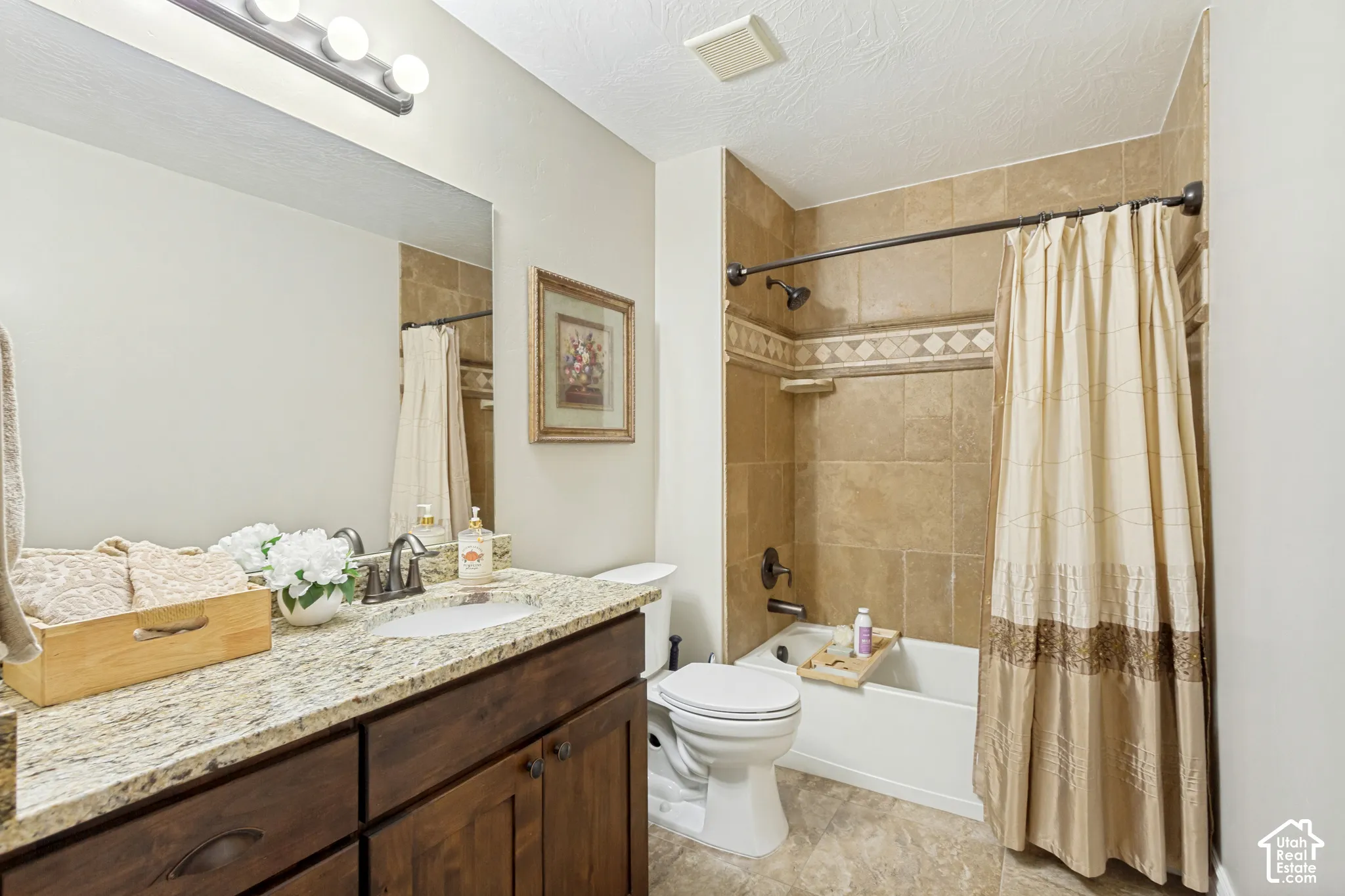 Bathroom featuring a vanity with granite countertop, undermount sink, dark-stained cabinetry, and a shower-tub combination with tiled surround and decorative tile inlay