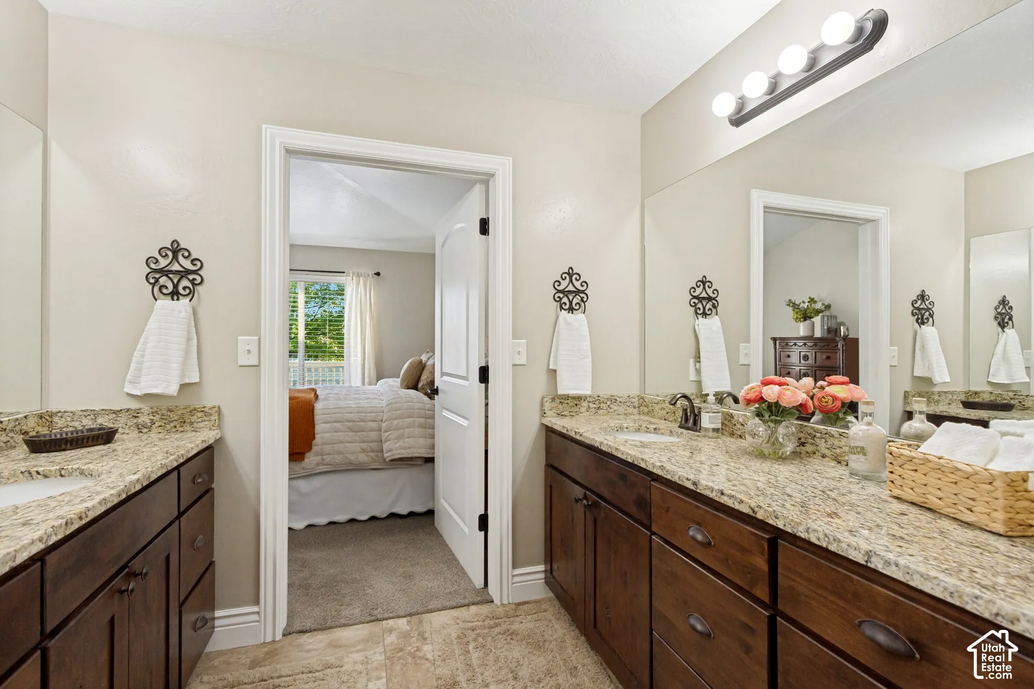 Dual-sink vanity with granite countertops, dark-finish cabinetry, tile flooring, and wall-mounted vanity lighting