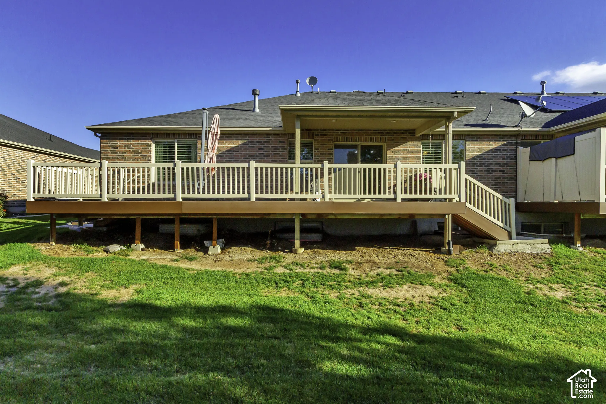 Rear exterior featuring a brick facade, elevated composite deck with white railings, a covered patio area, and sliding glass door access