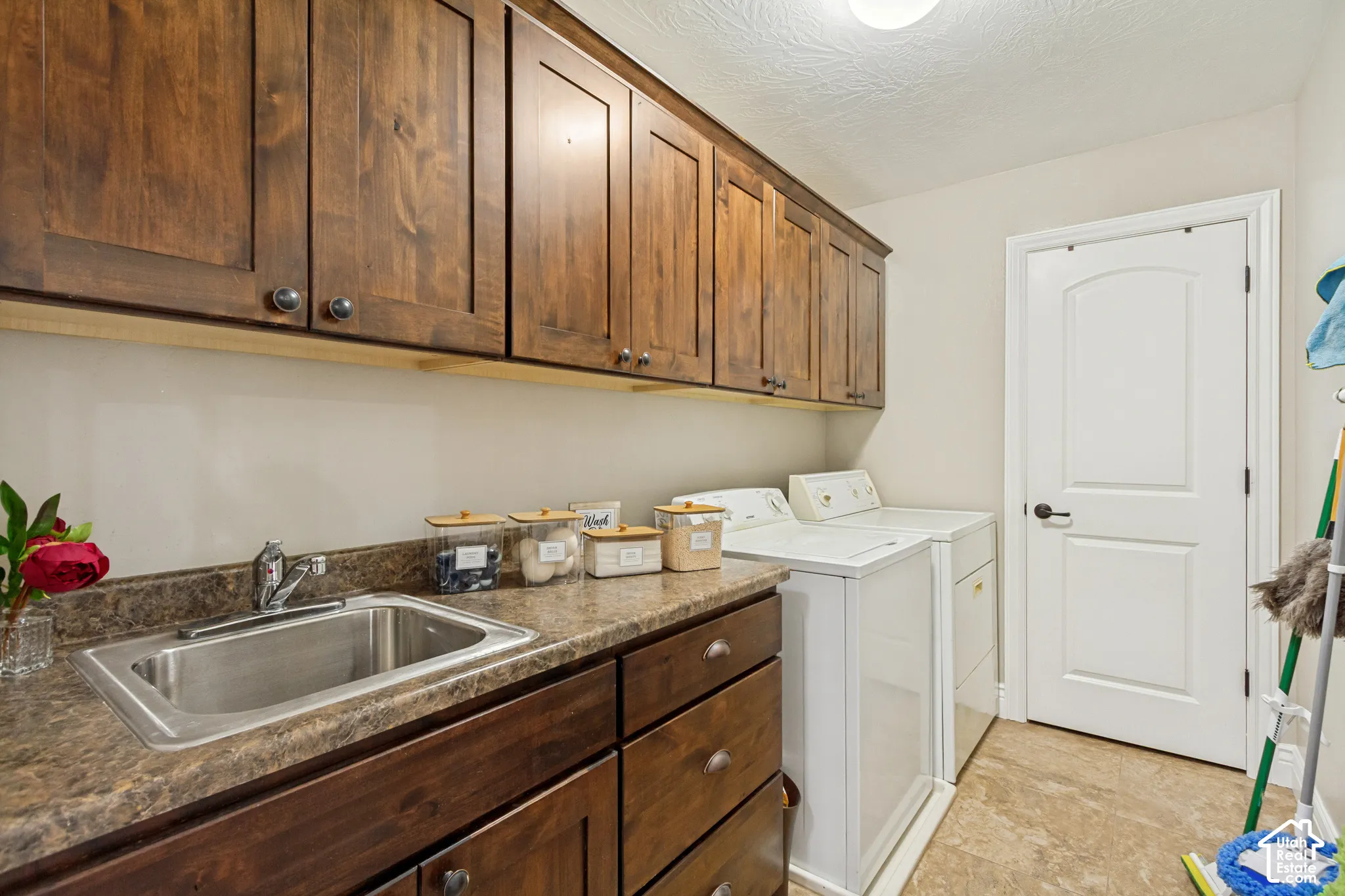 Laundry room featuring stained wood cabinetry, granite countertops, an integrated stainless steel drop-in sink, and tile flooring