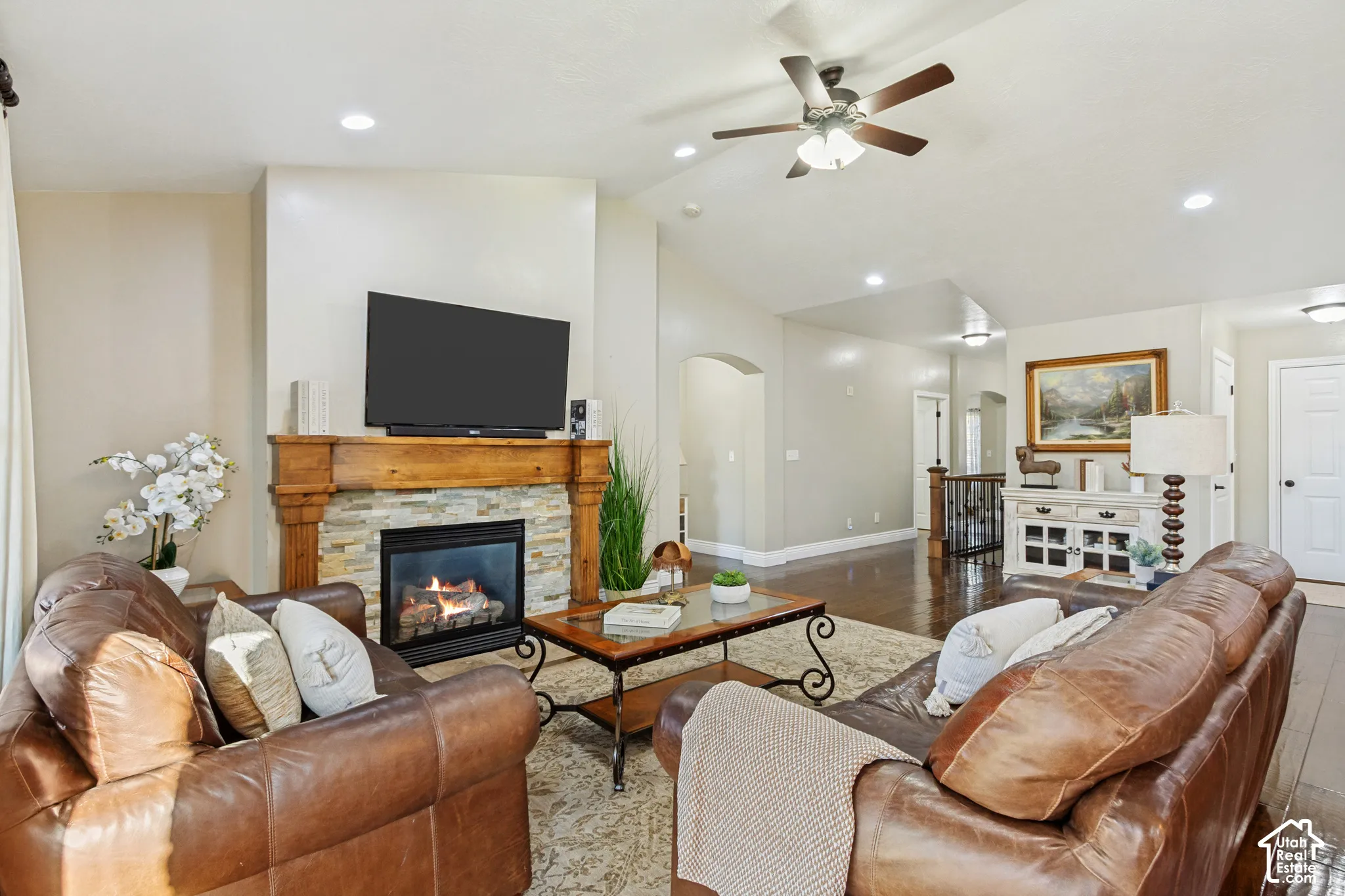 Vaulted ceiling with recessed lighting, hardwood flooring, and a fireplace featuring a stone surround and a substantial wood mantel