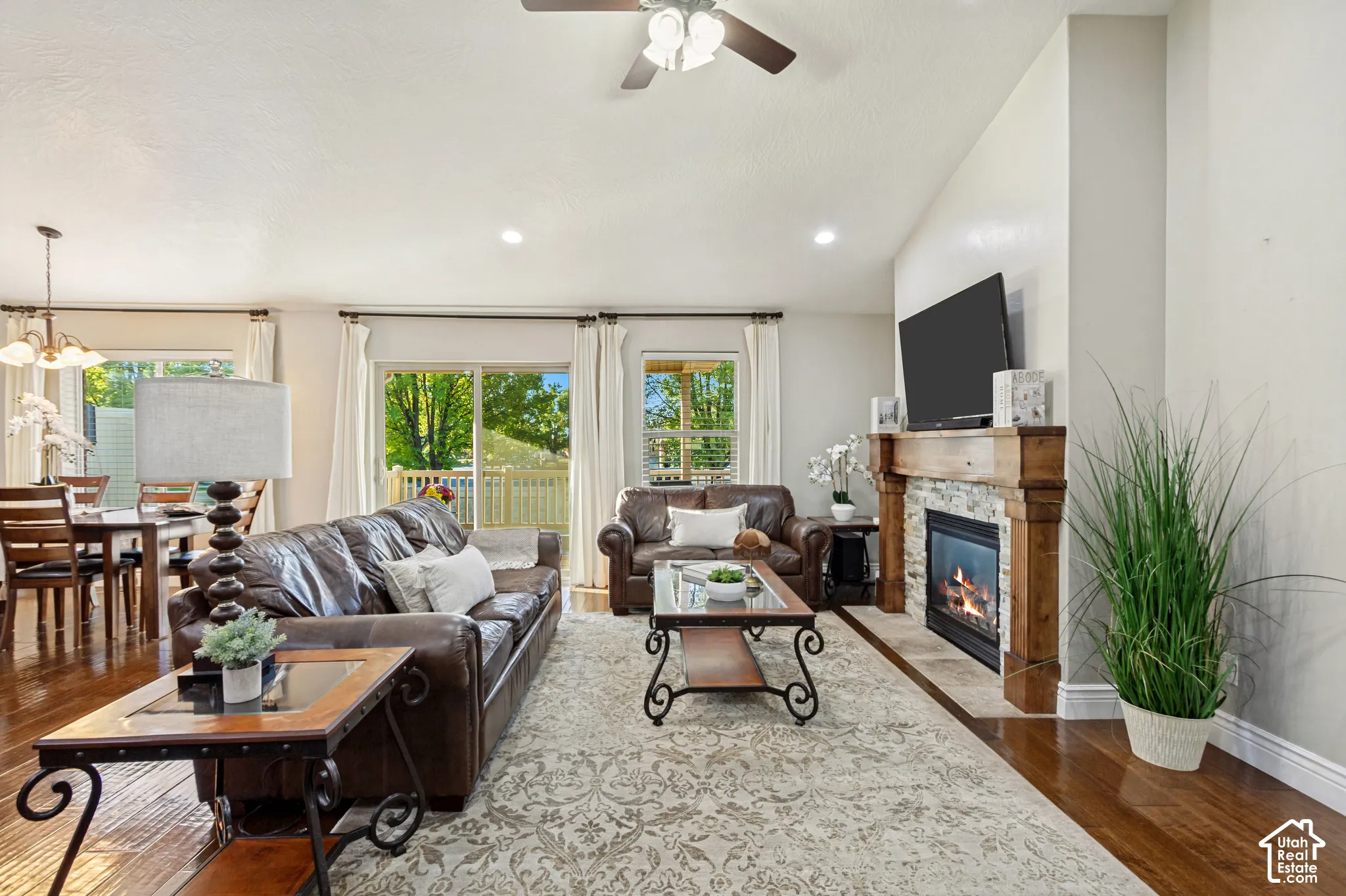 Living area featuring hardwood flooring, a stone-surround fireplace with a timber mantel, vaulted ceilings, recessed lighting, and a ceiling fan