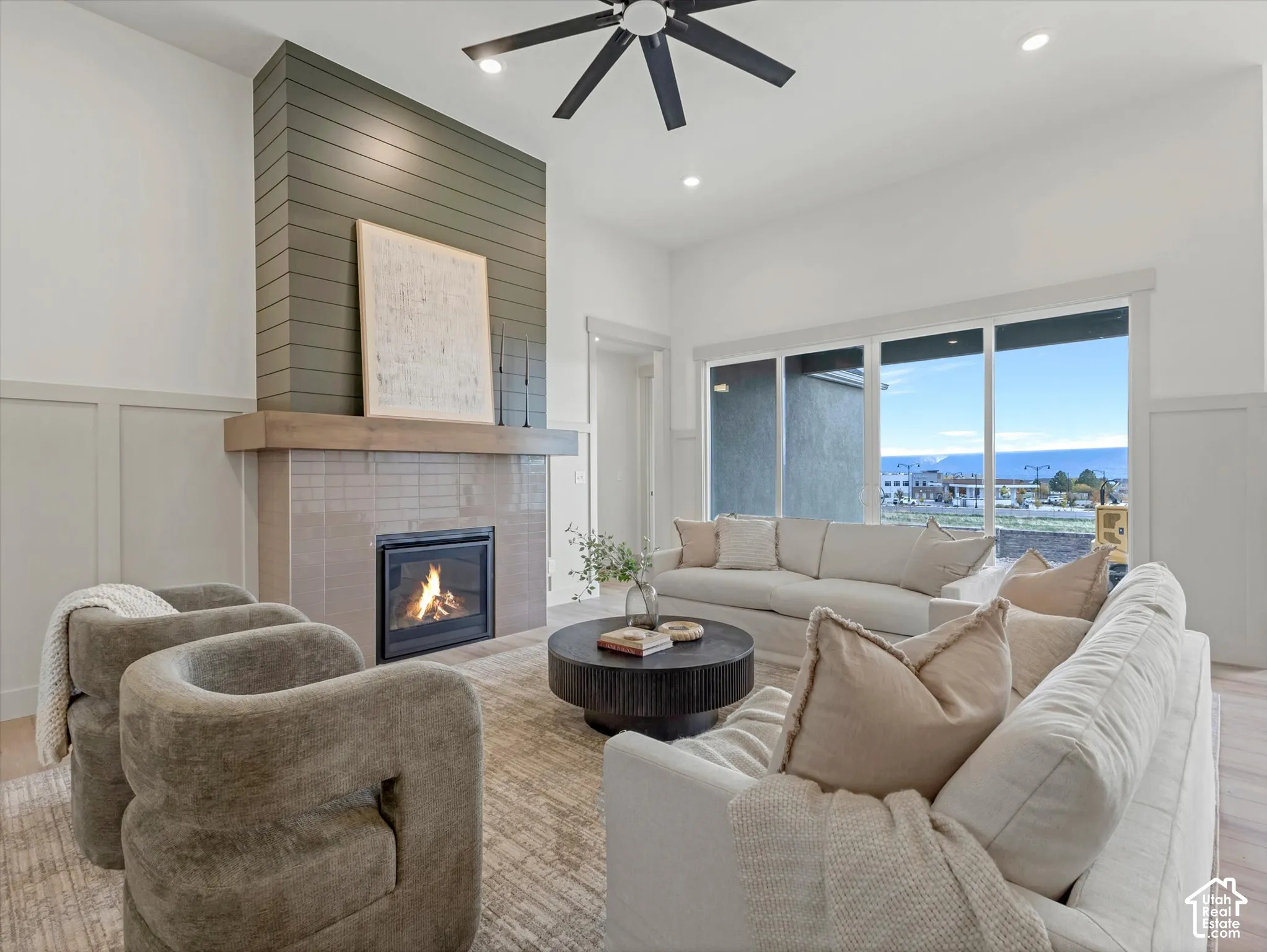 Vaulted ceilings with a ceiling fan, fireplace featuring a tile surround and wood mantel, shiplap accent wall, wood-finish flooring, and expansive windows