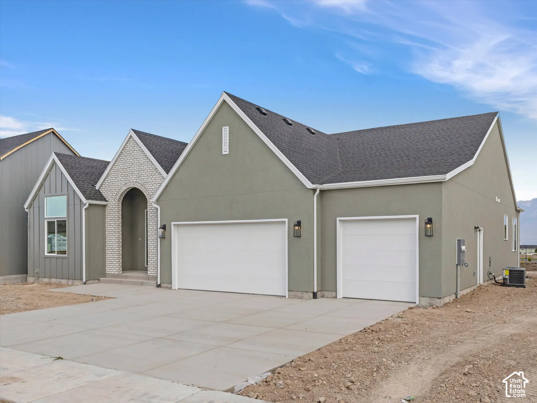 Single-level exterior featuring a stucco and brick facade, arched entryway, and attached three-car garage