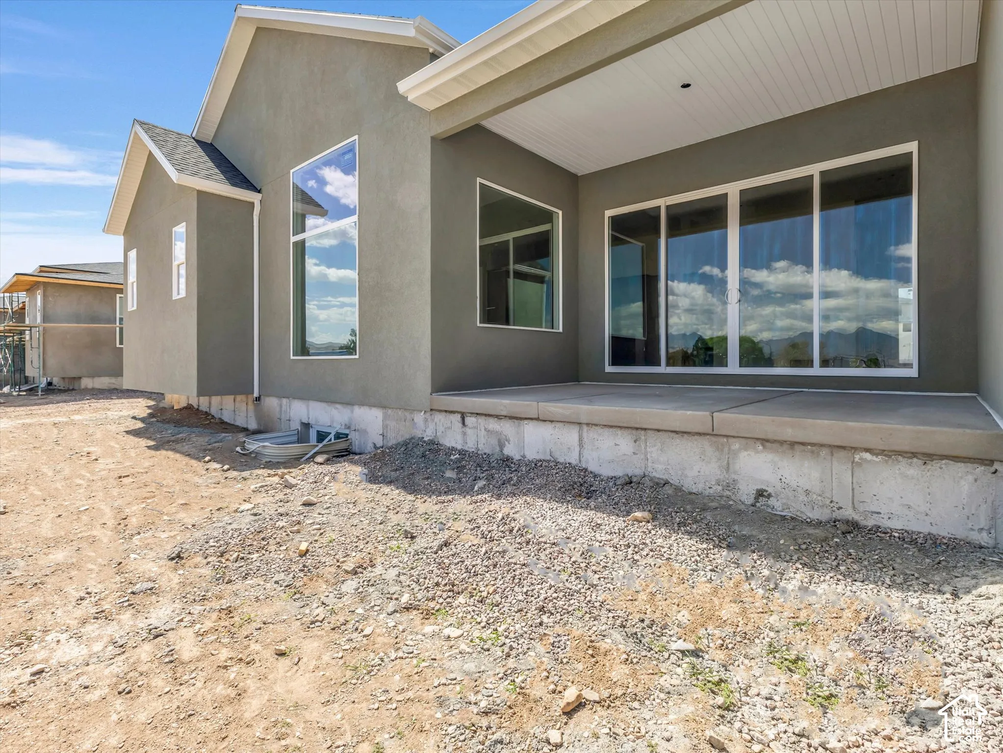 Covered rear patio featuring concrete foundation, stucco siding, large fixed-pane windows, and sliding glass door