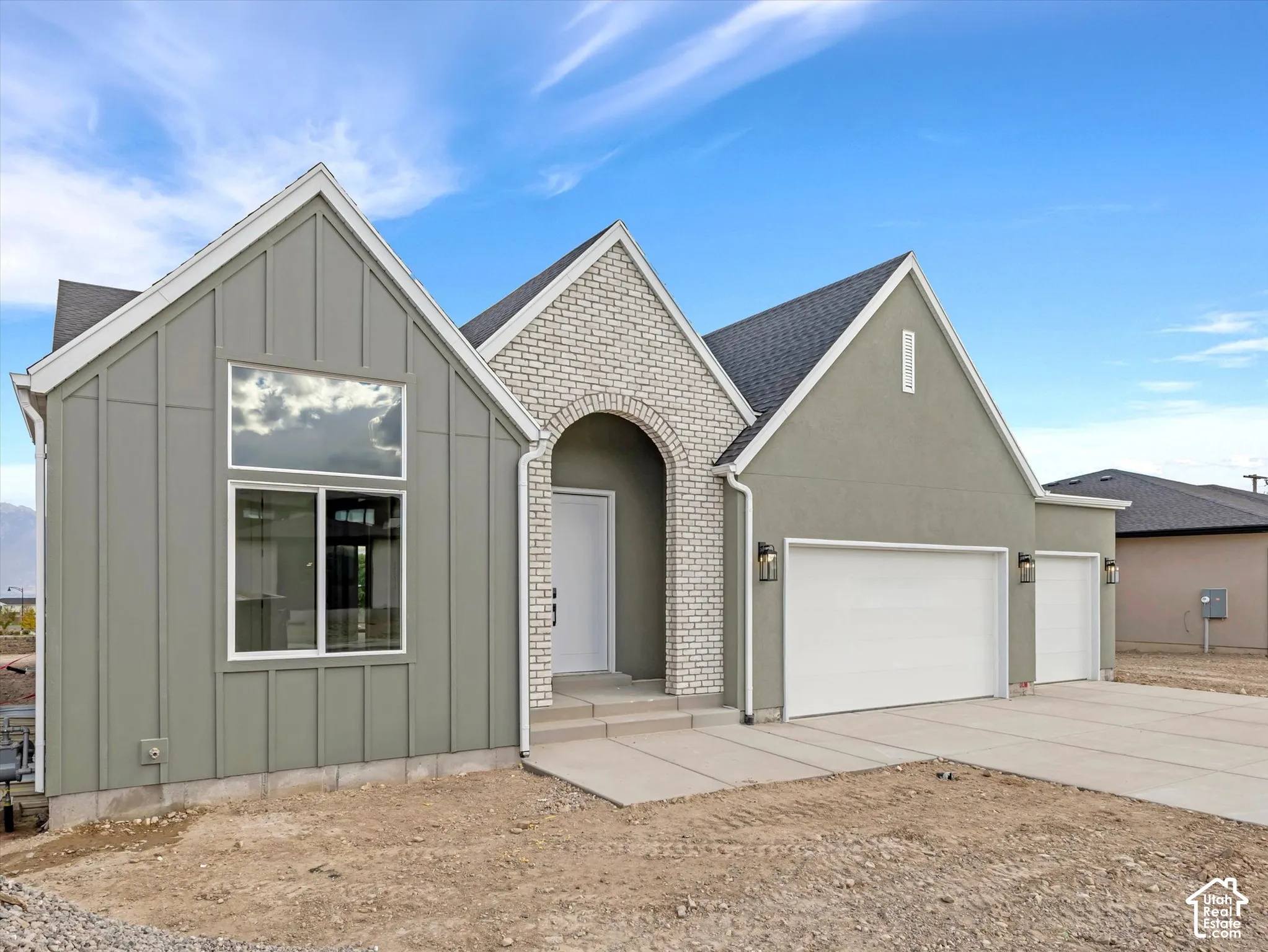 Modern exterior featuring vertical board-and-batten siding, arched brick entryway, multi-gabled roofline, and an attached three-car garage