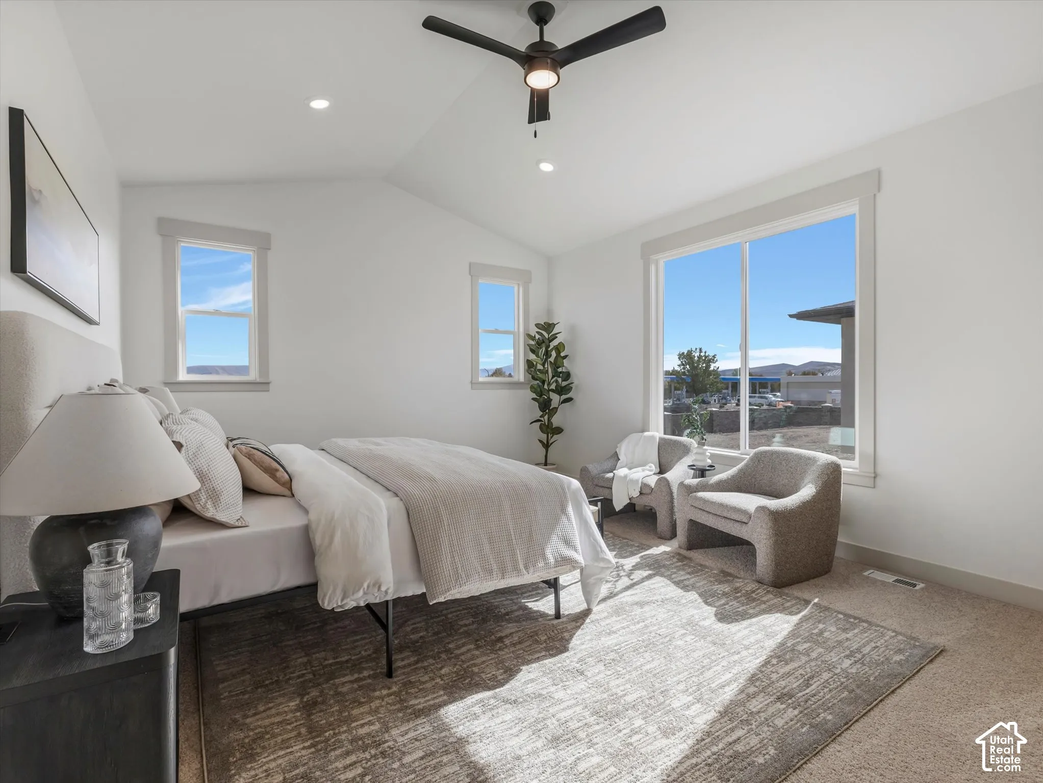 Vaulted ceilings featuring a dark-finish ceiling fan, multiple windows with neutral trim, and carpeting
