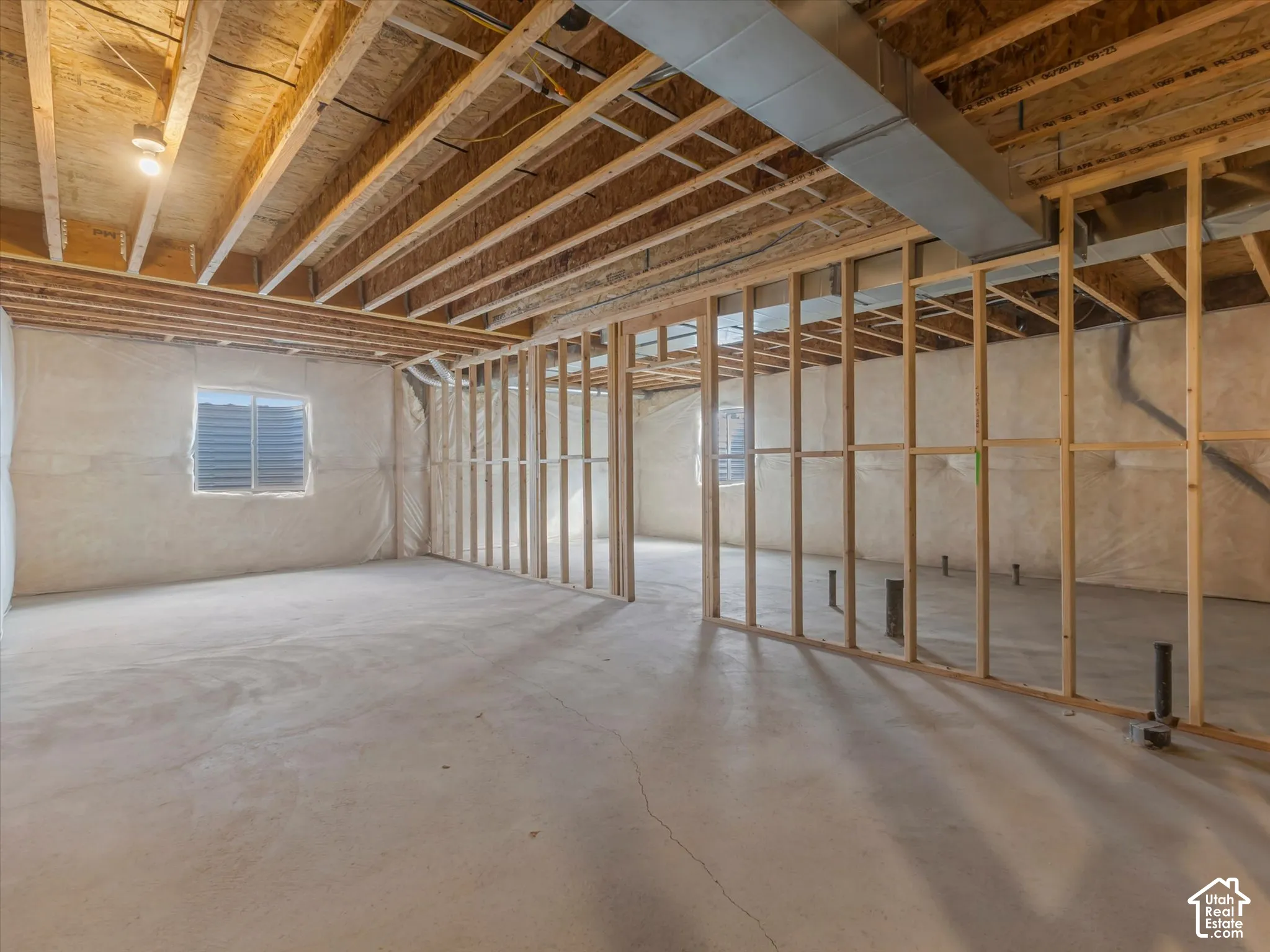 Unfinished interior space featuring exposed wood framing, concrete flooring, dual egress windows, and exposed ceiling joists with installed metal ductwork