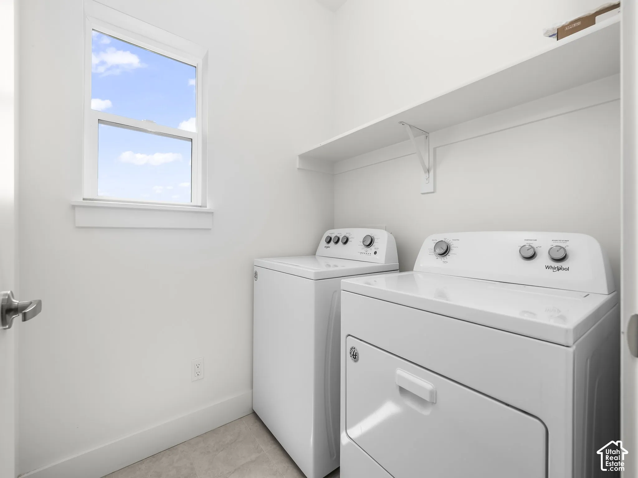 Laundry room featuring a single-hung window, built-in white overhead shelving, and neutral-tone flooring