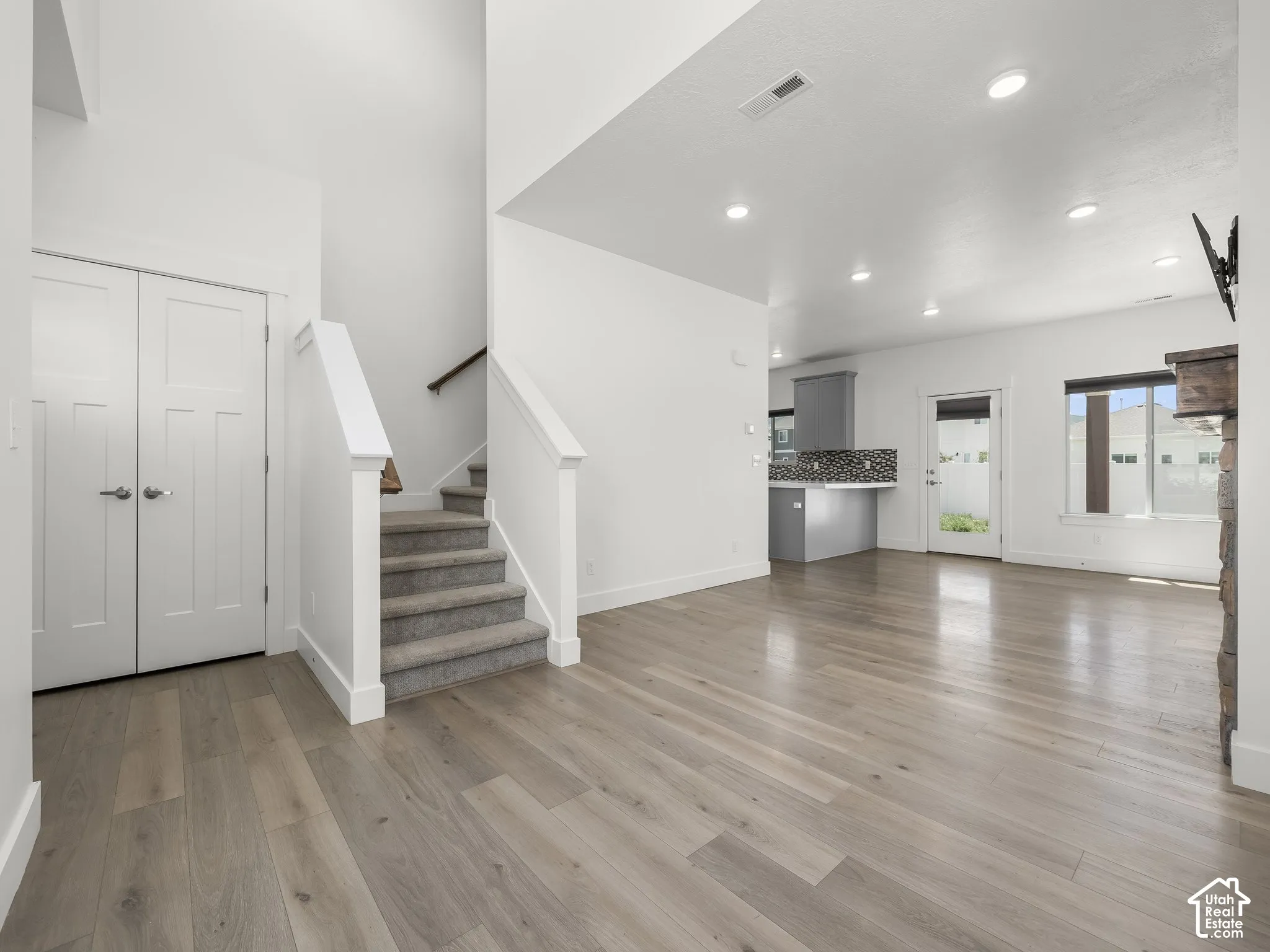 Open-concept interior featuring wood-finish flooring, recessed lighting, a fireplace with stone masonry surround, and a staircase with carpeted treads