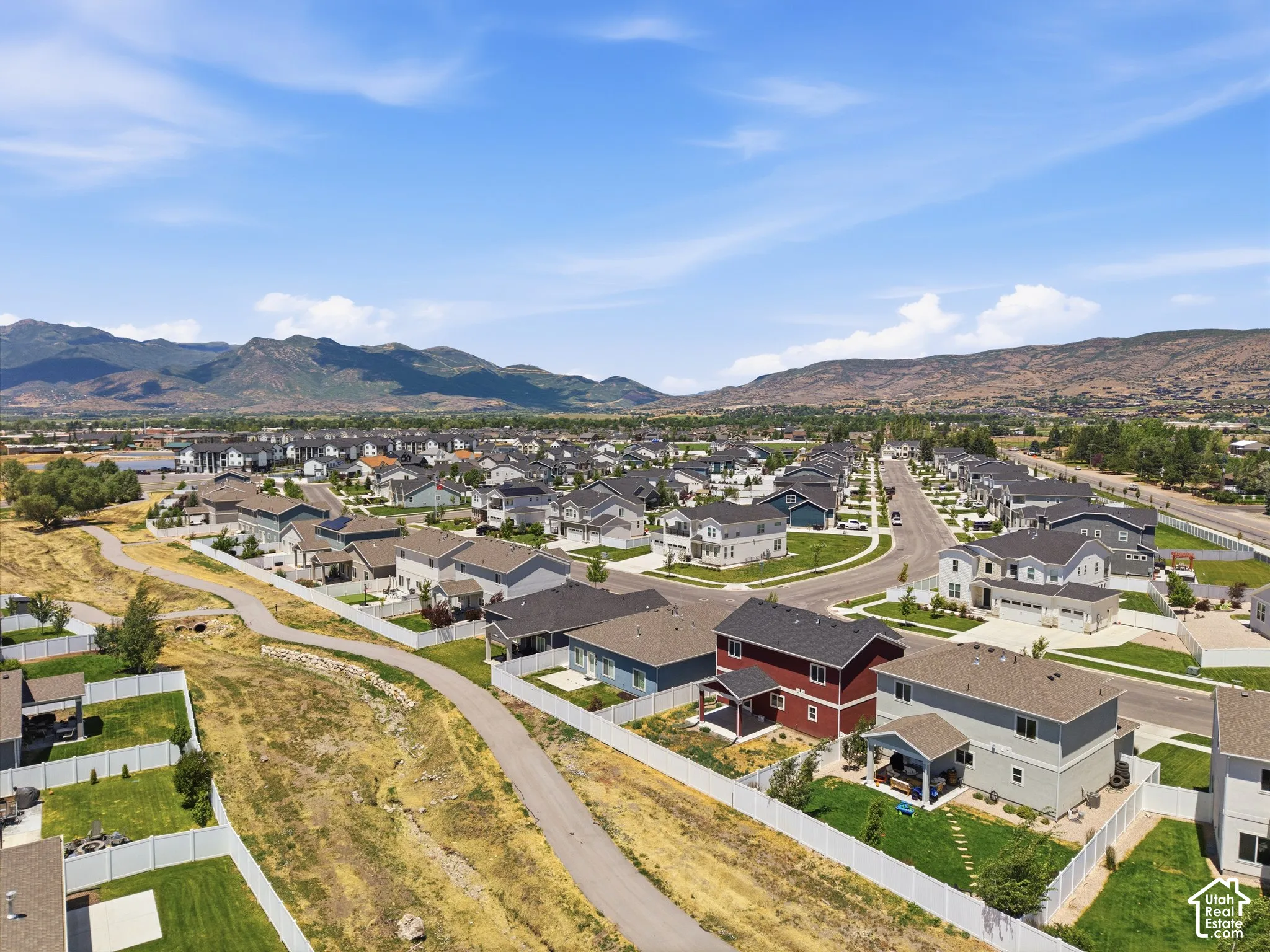 Aerial perspective featuring multi-story residential structures, paved streets, white perimeter fencing, manicured lawns, and a mountain backdrop