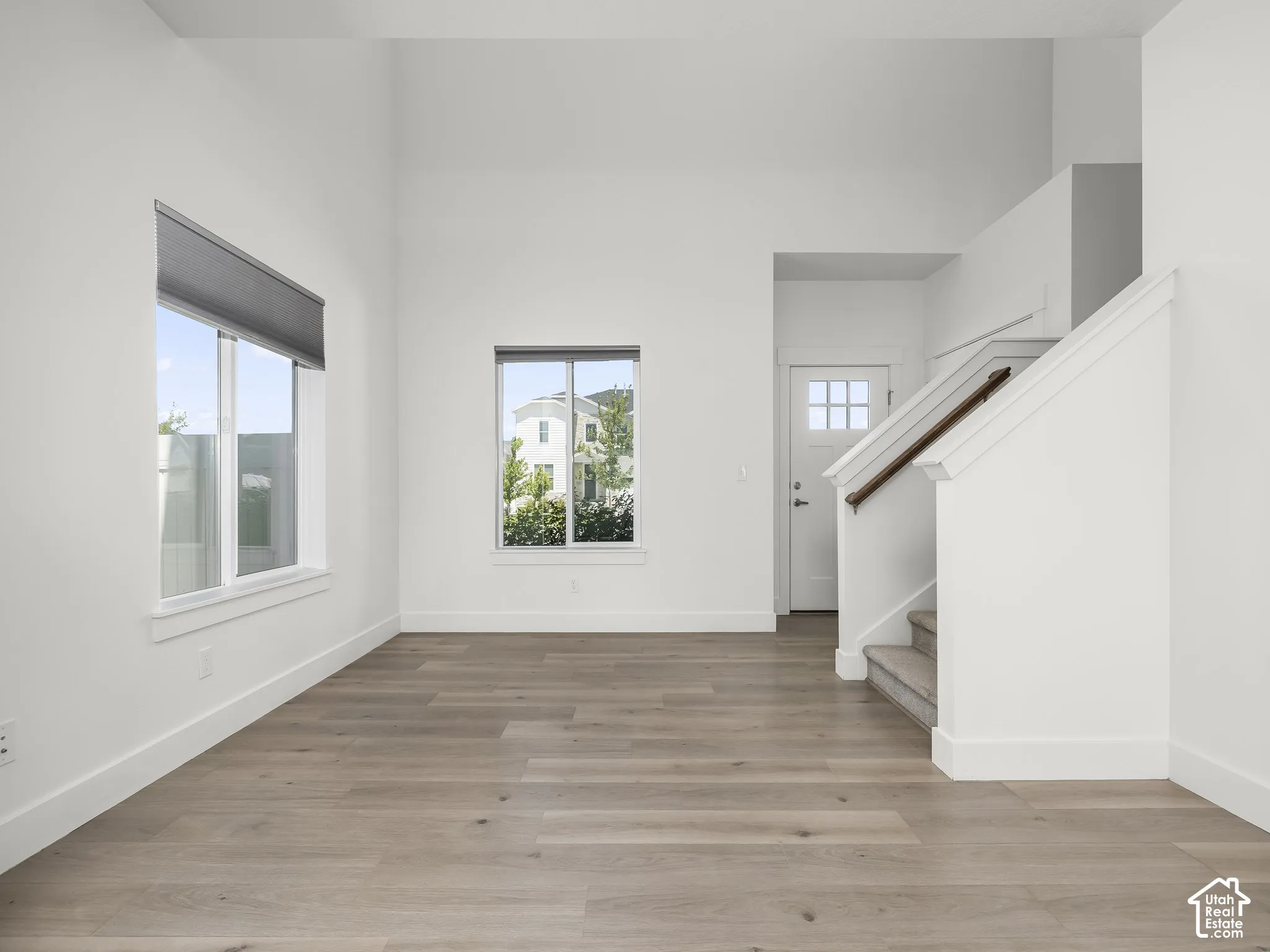 High-ceiling interior featuring wood-finish flooring, dual-pane windows, and a staircase with a wooden handrail