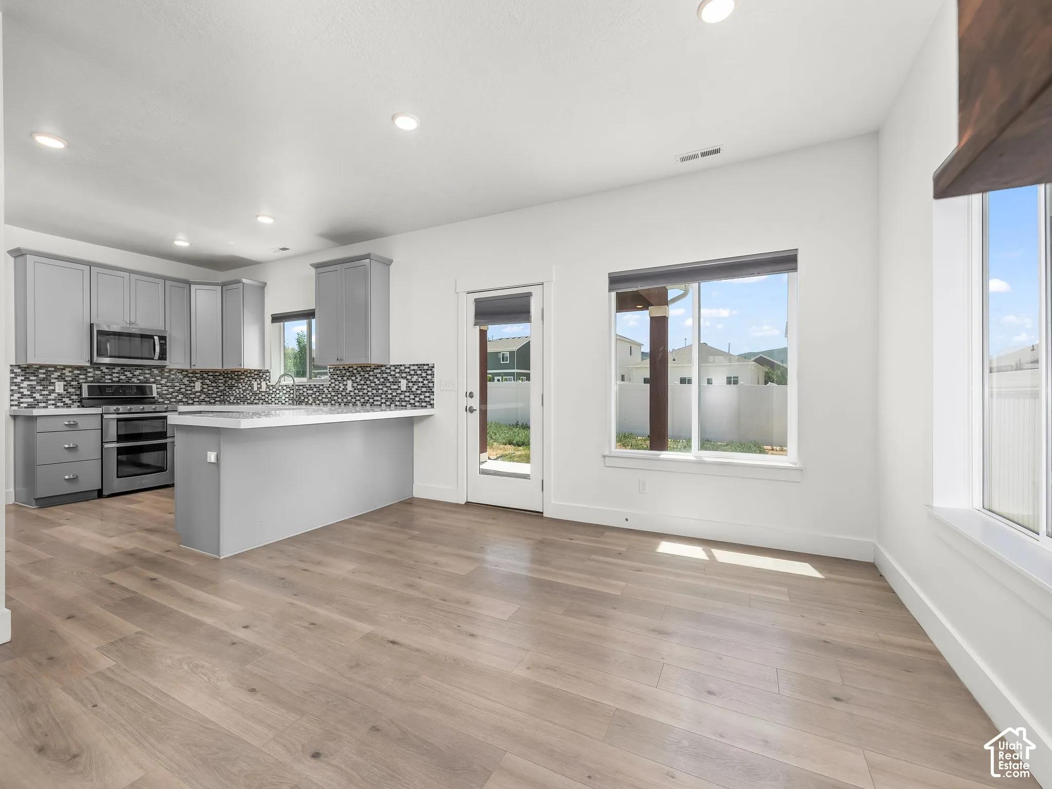 Kitchen featuring gray cabinetry, wood-finish flooring, a kitchen island, recessed lighting, and a mosaic tile backsplash