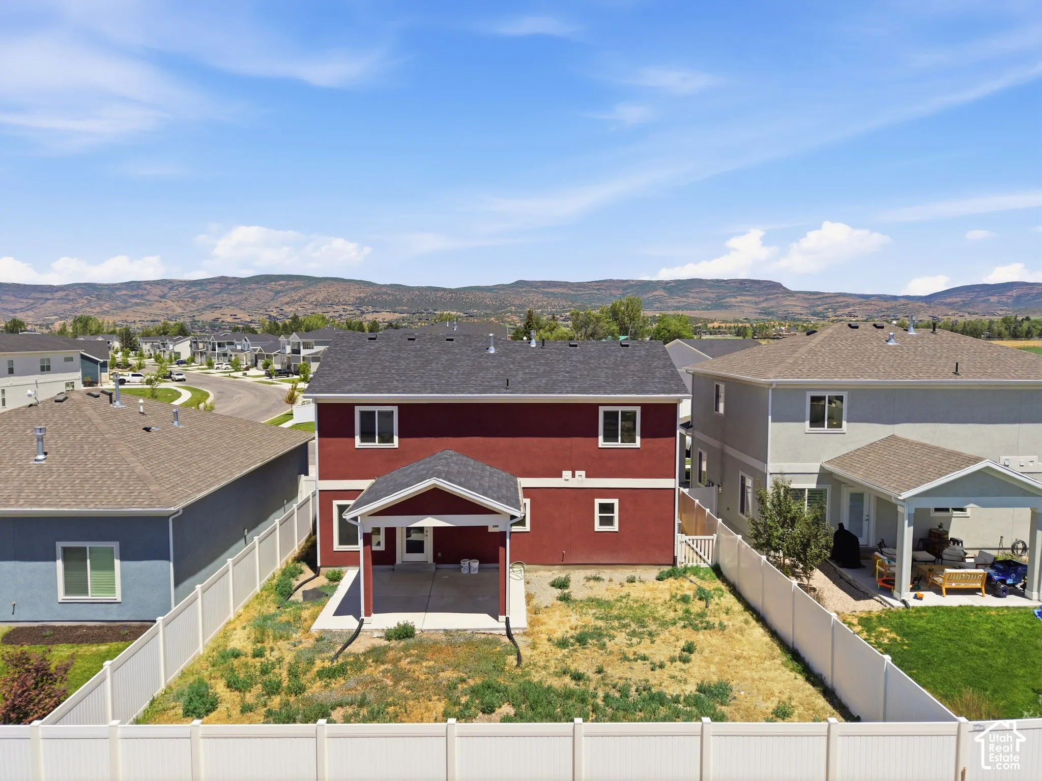 Two-story residence featuring a covered rear patio, white vinyl perimeter fencing, and mountain backdrop