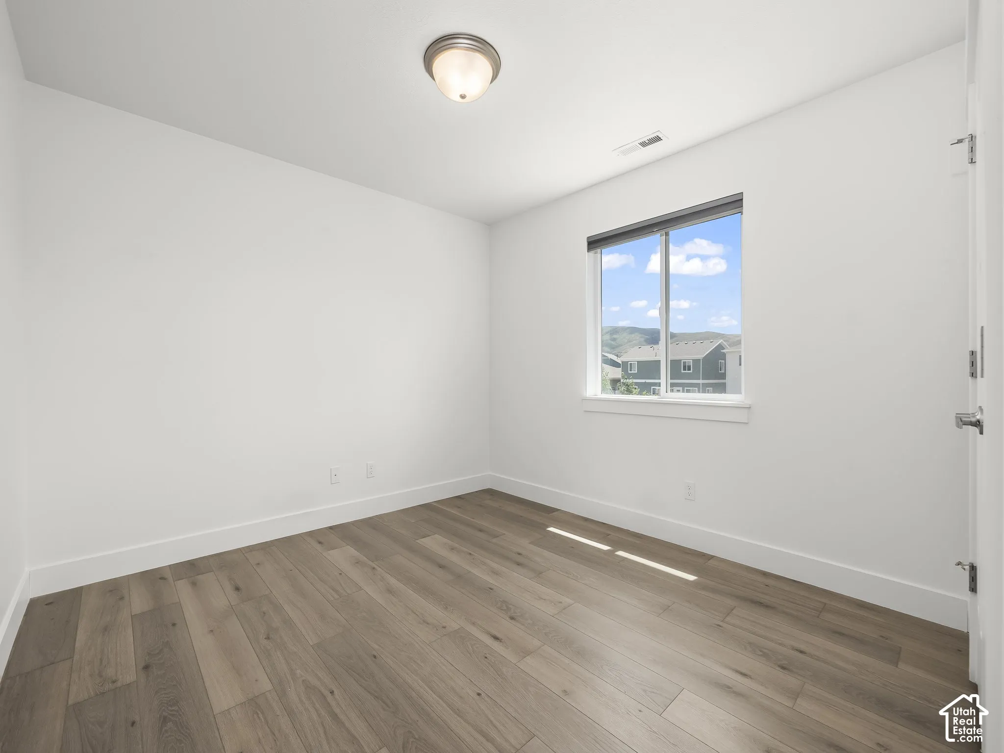 Room featuring wood-finish flooring, a single-pane window with a roller shade, and a flush-mount ceiling light fixture