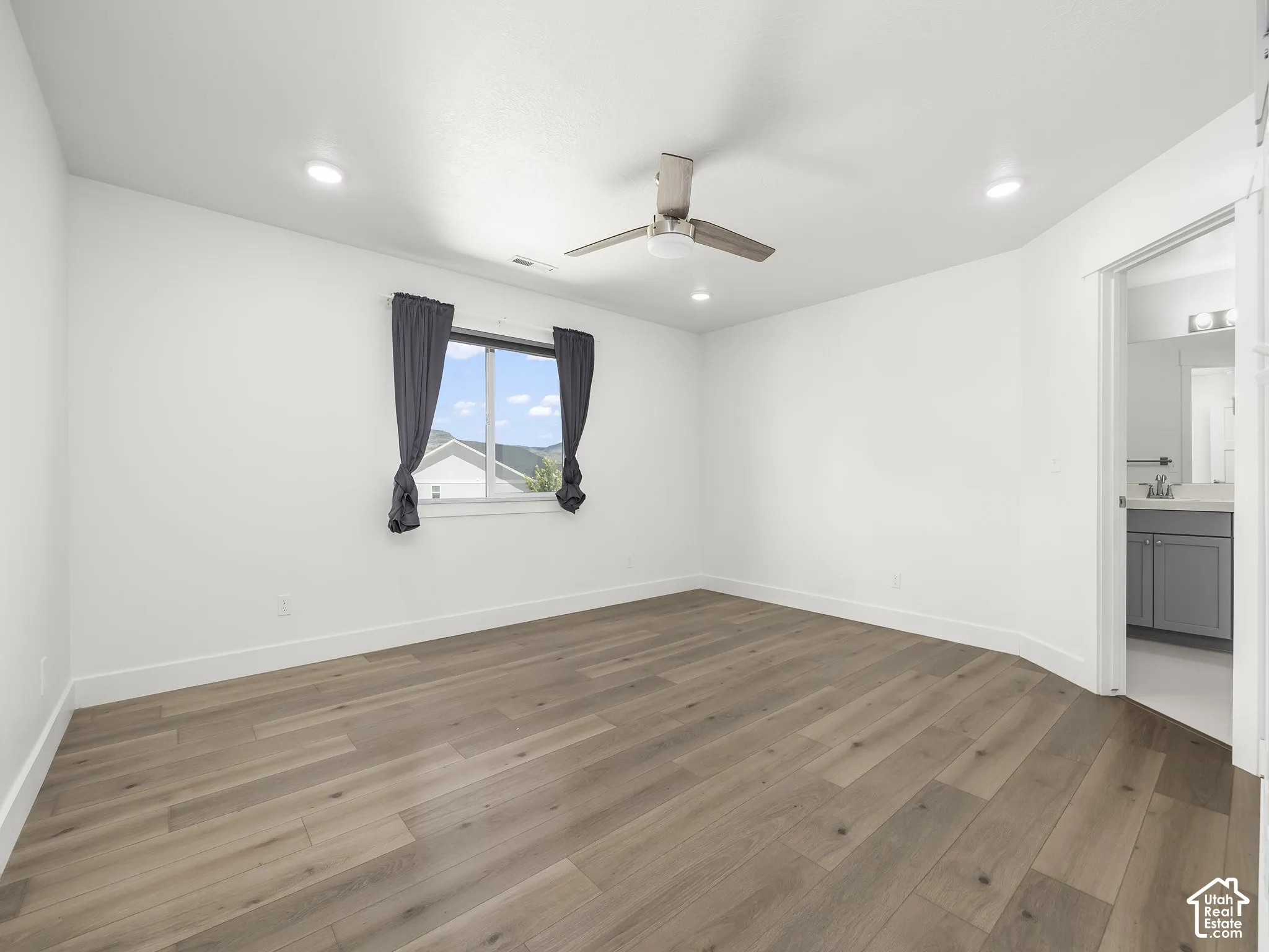Neutral-toned room featuring wood-finish flooring, recessed lighting, a modern ceiling fan, and a single-window configuration