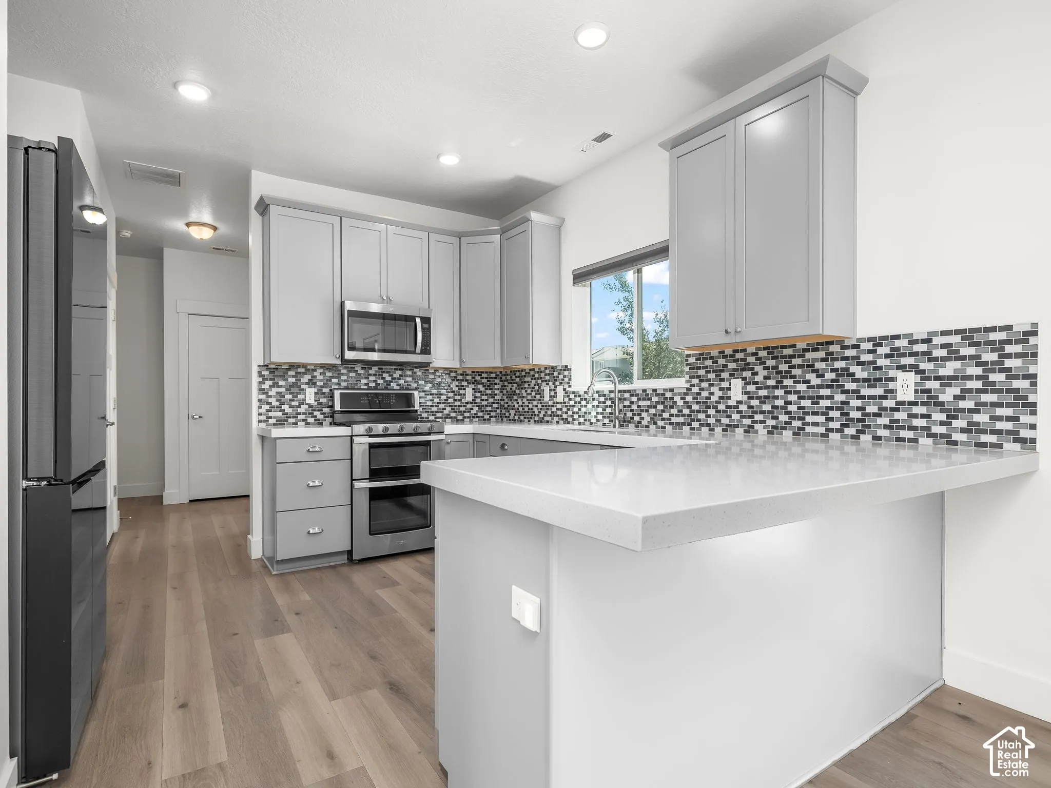 Kitchen featuring gray cabinetry, stone-finish countertops, a mosaic tile backsplash, stainless steel appliances, and wood-finish flooring