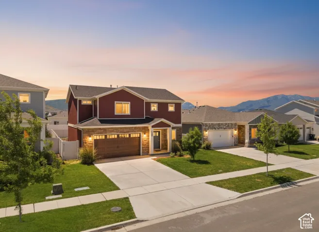 Two-story residence featuring horizontal siding, stone veneer accents, a multi-car garage with paneled doors, and concrete driveway