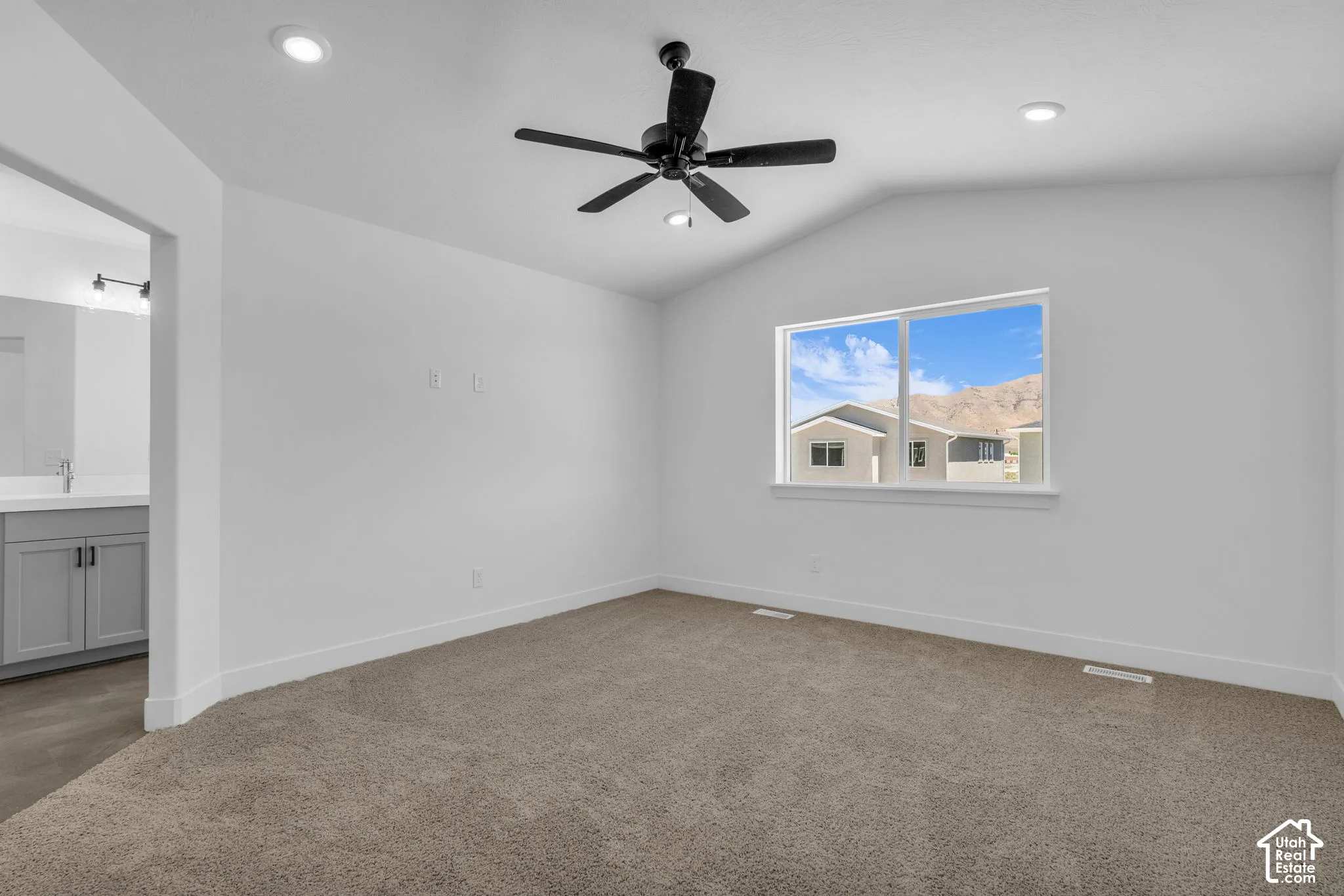 Primary bedroom with vaulted ceiling and ceiling fan adjacent to large walk-in closet as part of primary suite.