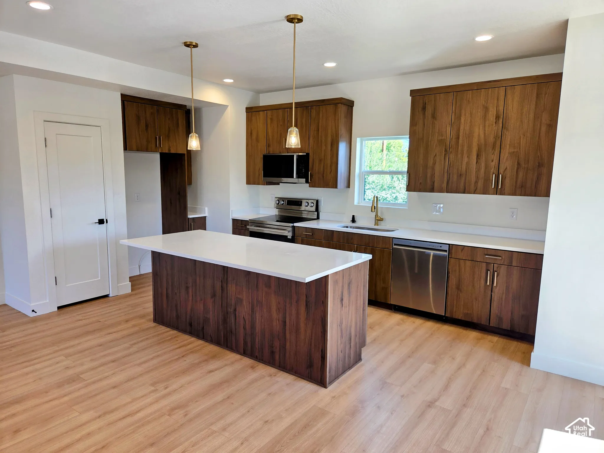 Kitchen featuring wood-finish cabinetry, white quartz countertops, a center island, stainless steel appliances, and wood-finish flooring