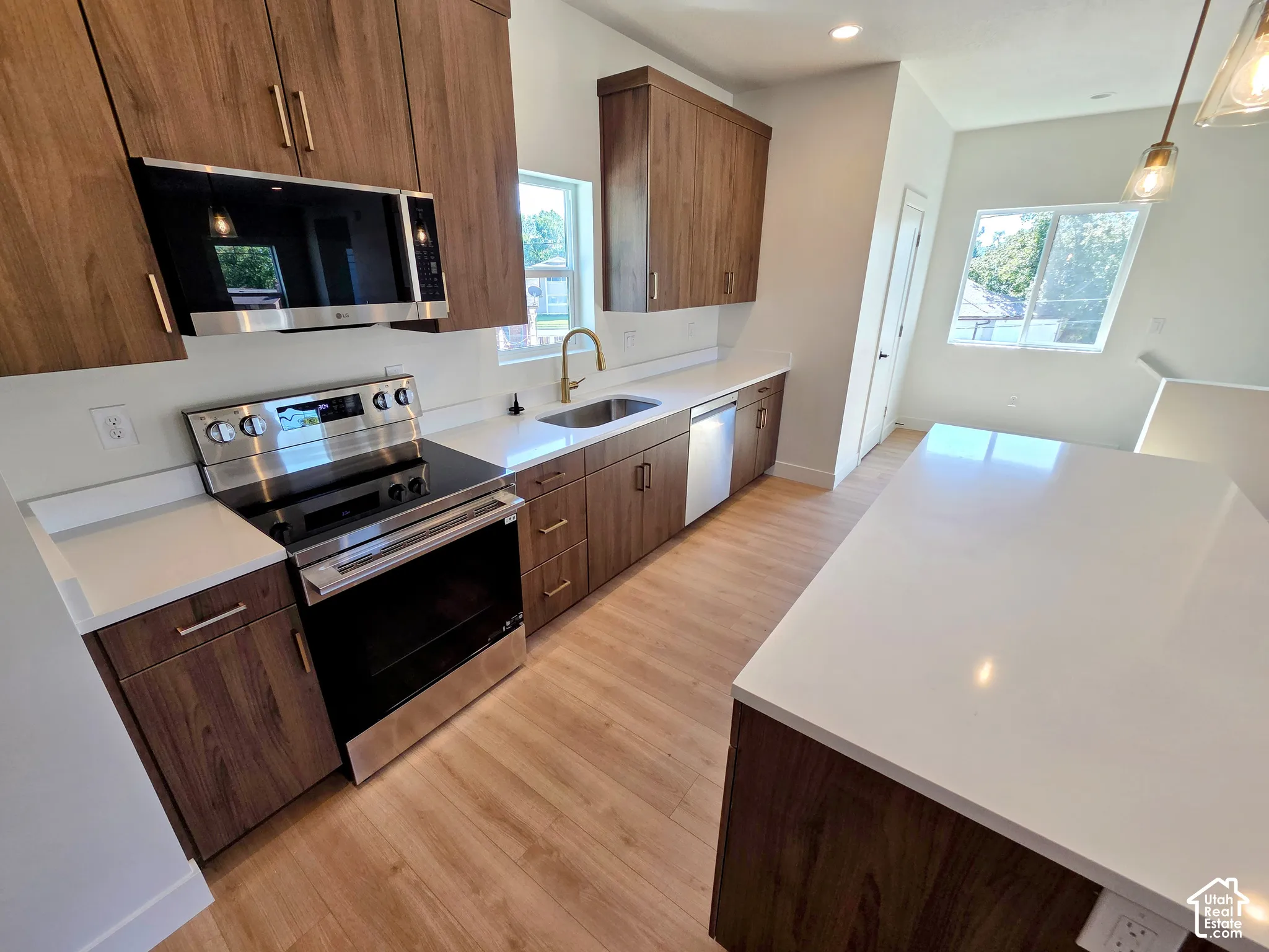 Kitchen featuring wood-finish cabinetry, quartz countertops, a stainless steel electric range, an undermount sink with a brass-finish faucet, and wood-finish flooring