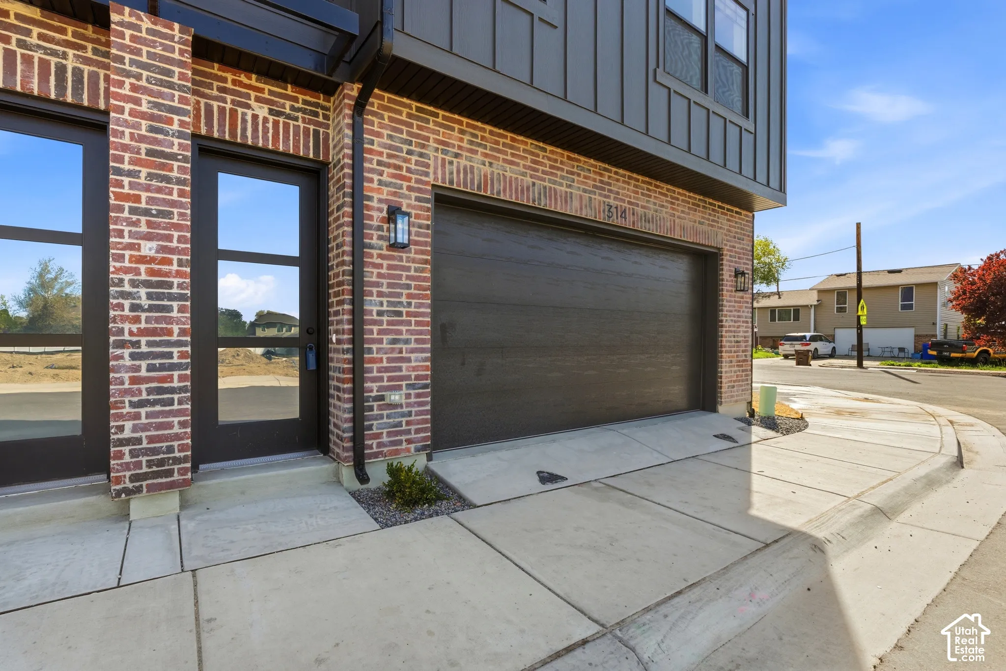 Brick exterior with dark siding accents, a dark paneled garage door, and a modern glass-paneled entry door