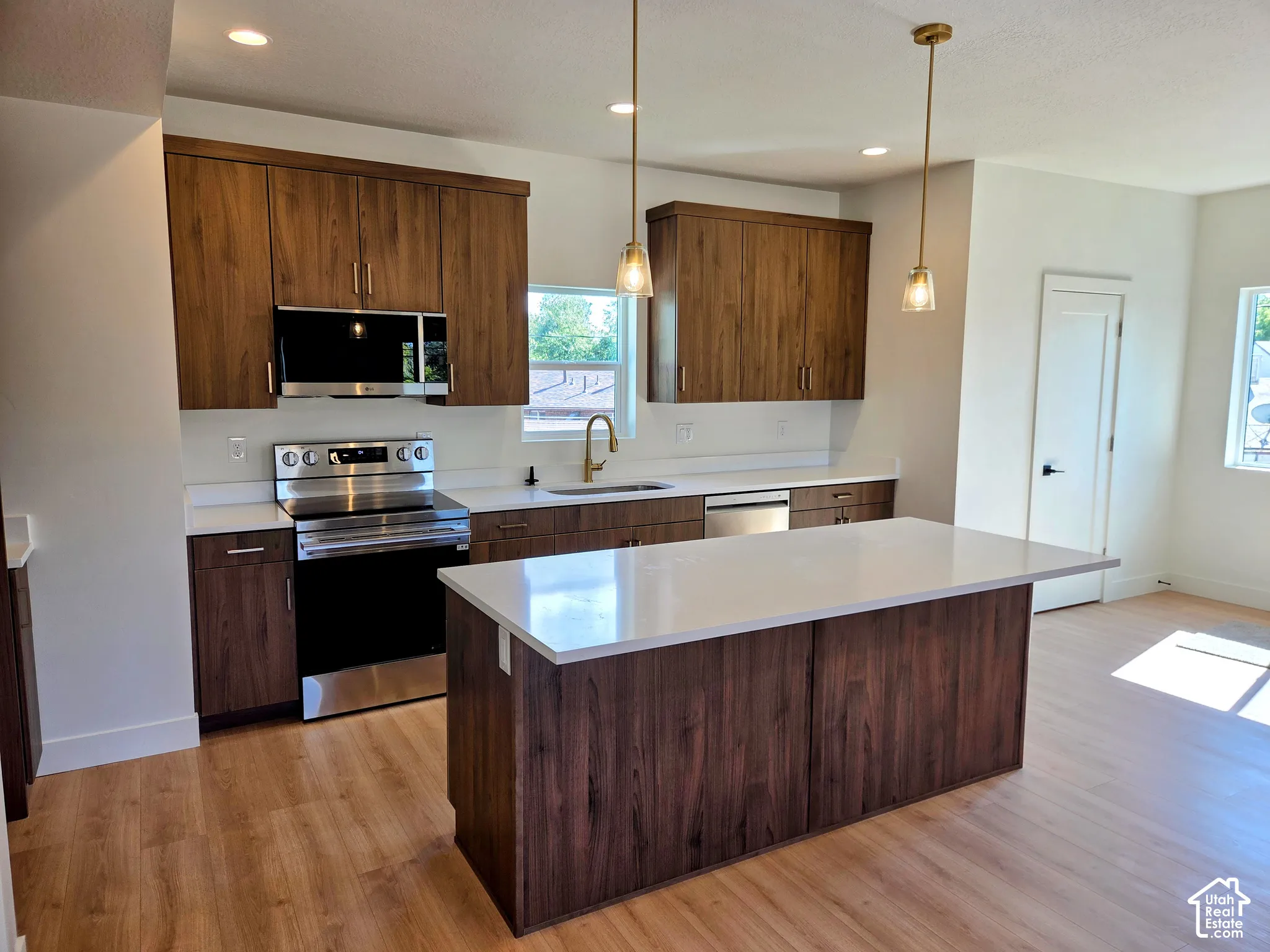 Kitchen featuring wood-finish cabinetry, a central island with a quartz countertop, stainless steel appliances, and pendant lighting