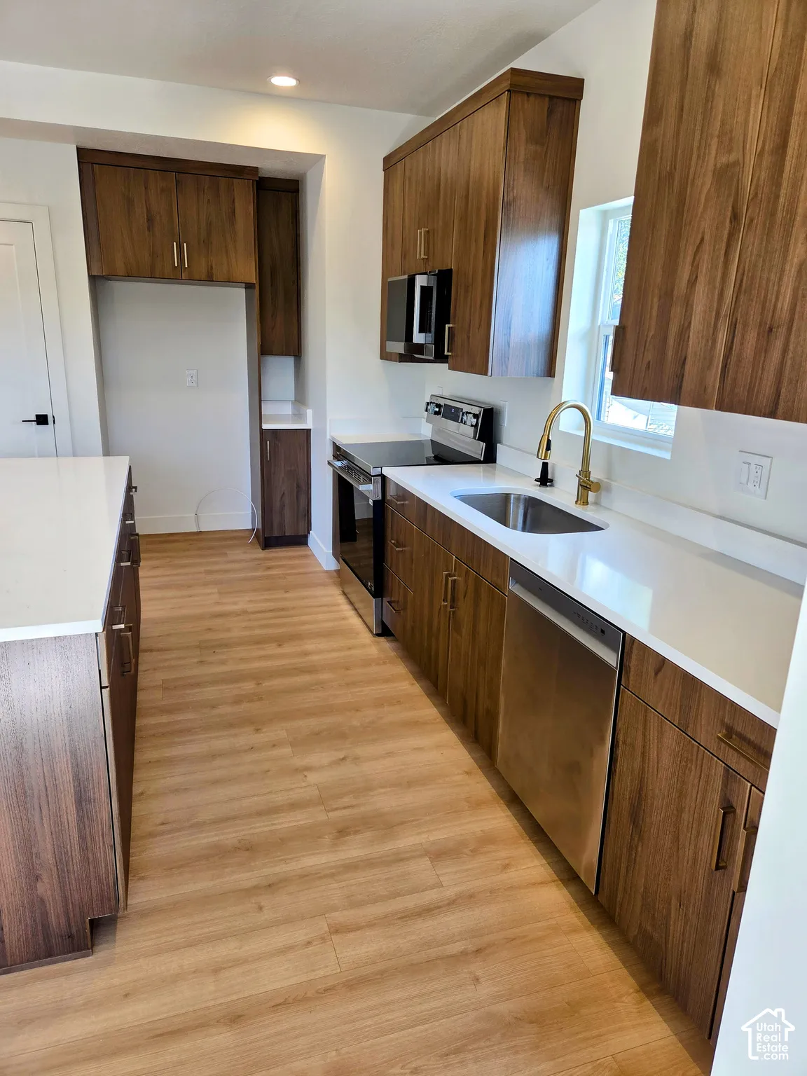 Kitchen featuring wood-finish cabinetry, quartz countertops, an island, wood-finish flooring, and stainless steel appliances