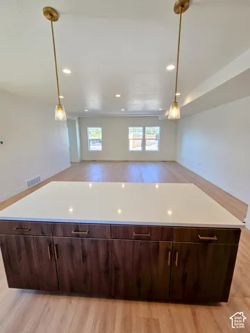 Kitchen island with white solid-surface countertop, dark wood-tone cabinetry, brushed gold hardware, and dual pendant lighting fixtures above wood-finish flooring