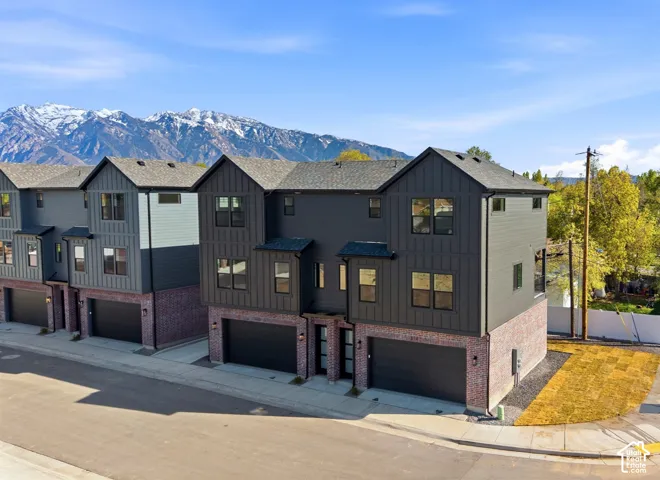 Multi-story exterior featuring dark vertical siding, red brick masonry, attached garages, and a mountain backdrop