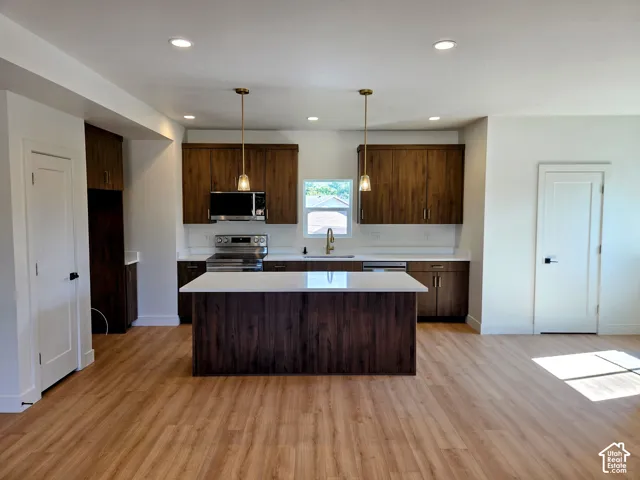 Kitchen featuring wood-finish cabinetry, a central island with a quartz countertop, wood-finish flooring, recessed lighting, and brass-finish pendant fixtures