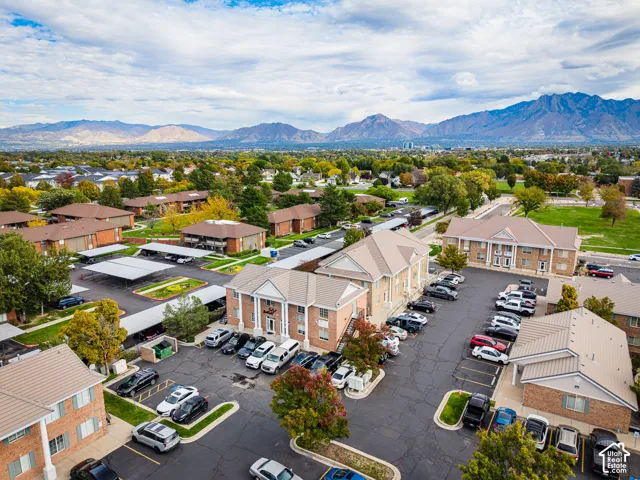 Aerial perspective of a multi-building residential community featuring brick and siding exteriors, pitched roofs, covered parking structures, and a mountain backdrop