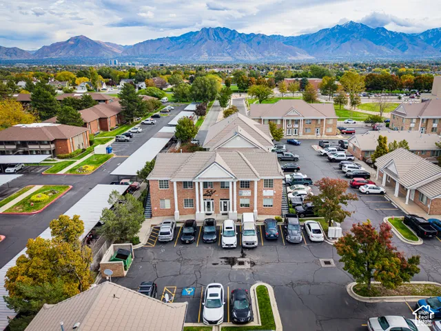 Multi-unit brick exterior featuring a prominent gabled portico with columns, paved parking areas, and mountain scenery