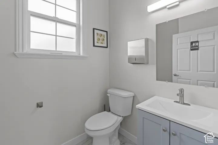 Restroom featuring a vanity with a rectangular sink, brushed nickel faucet, wall-mounted light fixture, single-hung window with casing, and tiled flooring