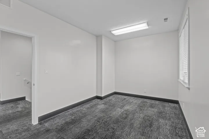 Room featuring neutral-toned carpeting, high-contrast dark trim, bright recessed rectangular lighting, and a window with horizontal blinds