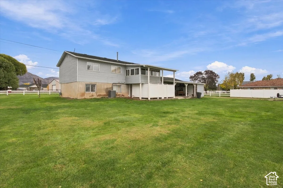Expansive backyard featuring a large grass lawn, white perimeter fencing, an elevated porch, and a covered patio area