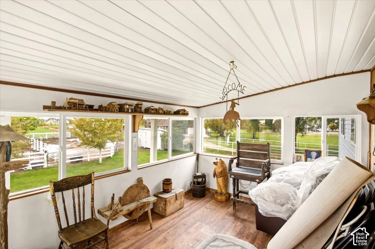 Enclosed sunroom featuring wood-finish flooring, white beadboard ceiling, and expansive windows with exterior rural scenery