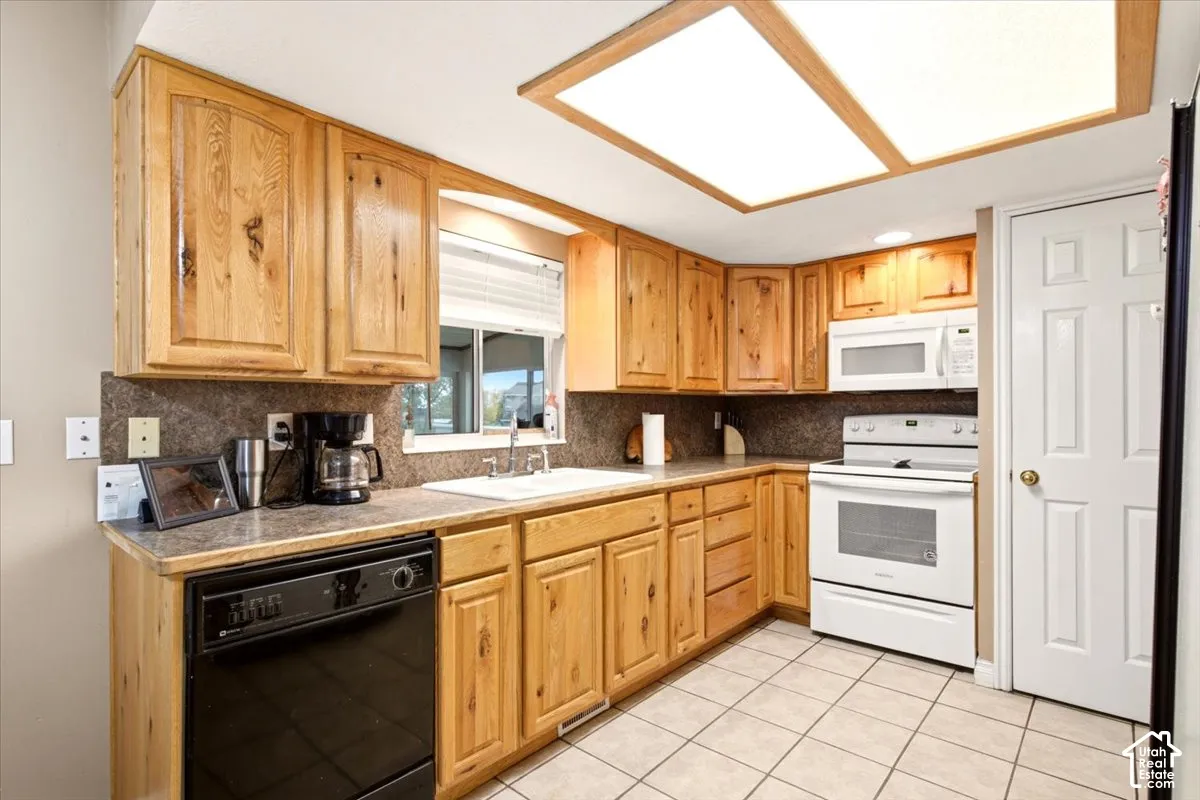 Kitchen featuring natural wood cabinetry, solid surface countertops, tile flooring, integrated lighting, and white appliances