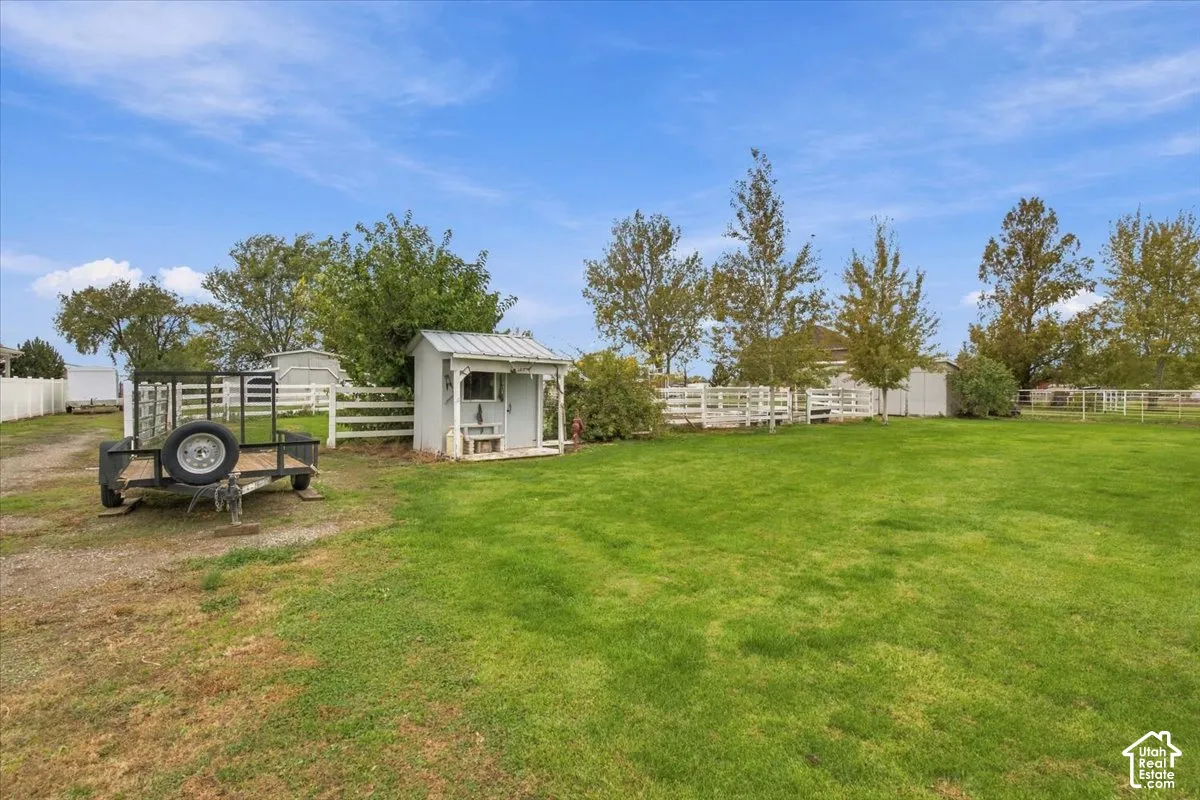 Expansive lawn featuring perimeter white rail fencing, mature trees, and a detached outbuilding with a metal roof