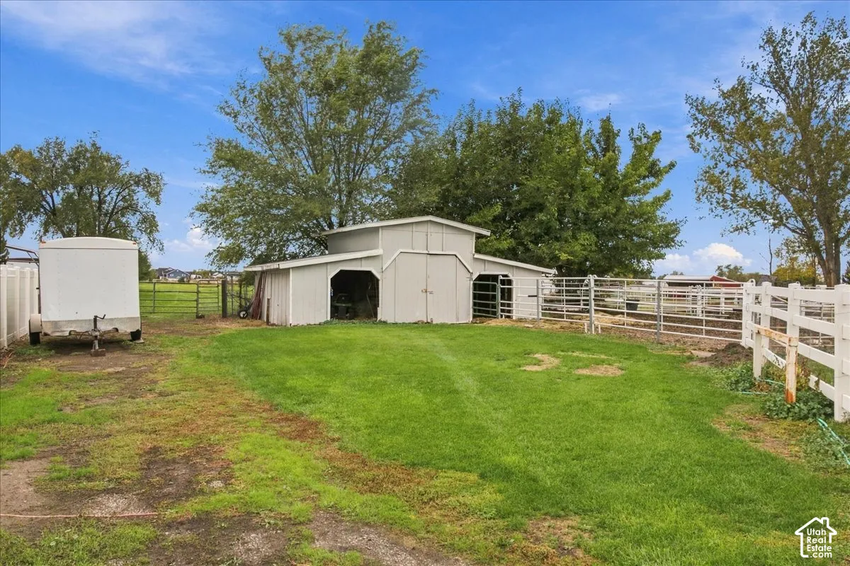 Outbuilding featuring double-door entry and two side stalls, complemented by fenced pasture space and white vinyl perimeter fencing