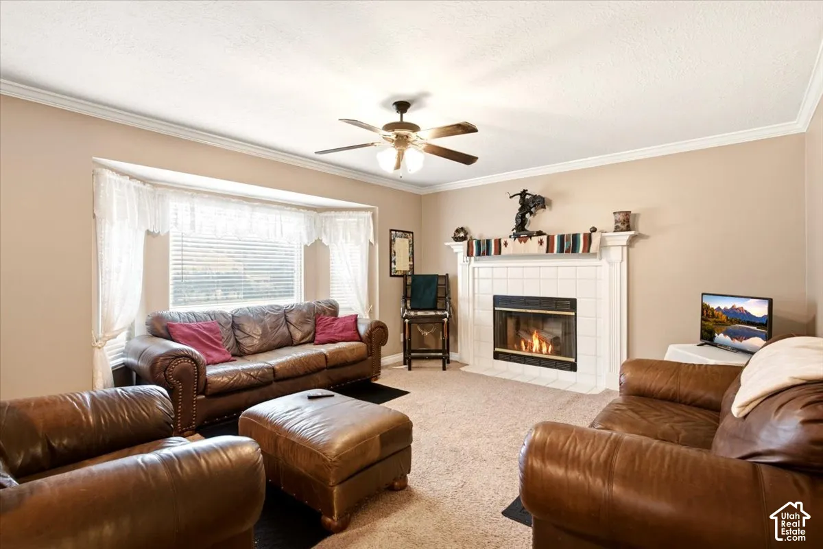 Fireplace with a white mantel and tile surround, bay window, ceiling fan with integrated light fixture, and crown molding
