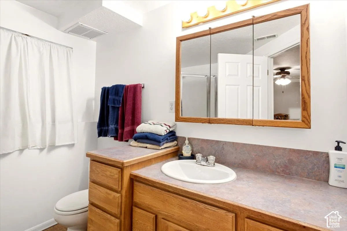 Bathroom featuring a vanity with oak cabinetry, multi-tonal countertop, inset oval basin, chrome-finish widespread faucet, and a tri-fold medicine cabinet with an integrated light fixture