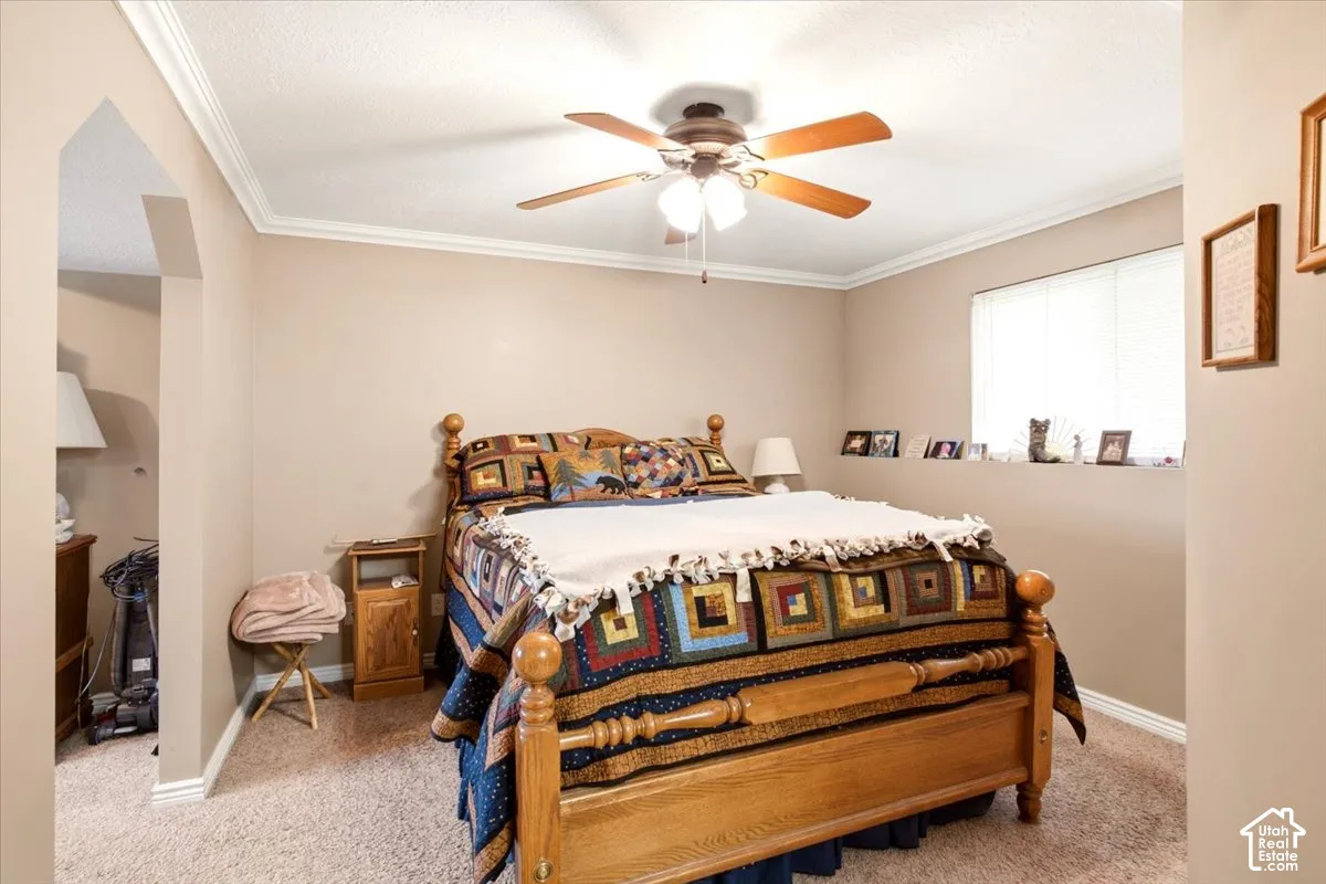 Bedroom interior featuring crown molding, neutral wall paint, a ceiling fan with integrated lighting, and a built-in recessed wall alcove