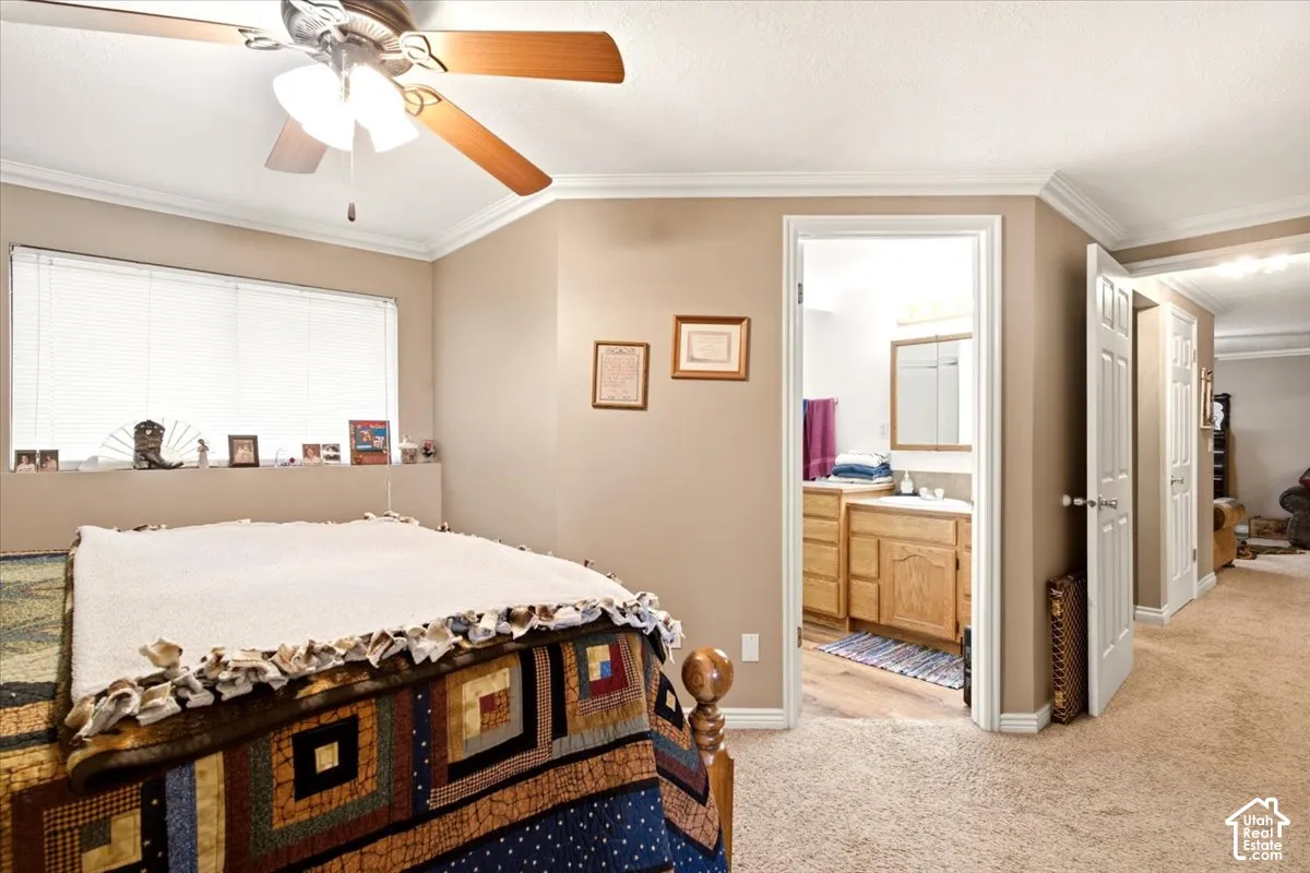Bedroom featuring a ceiling fan with integrated lighting, neutral wall paint, and crown molding, with an entry to a bathroom containing a vanity with wood cabinetry and a wood-finish floor
