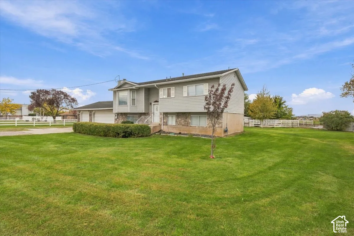 Exterior featuring light-gray horizontal siding, stone masonry accents, a multi-car garage, and a expansive lawn enclosed by white rail fencing