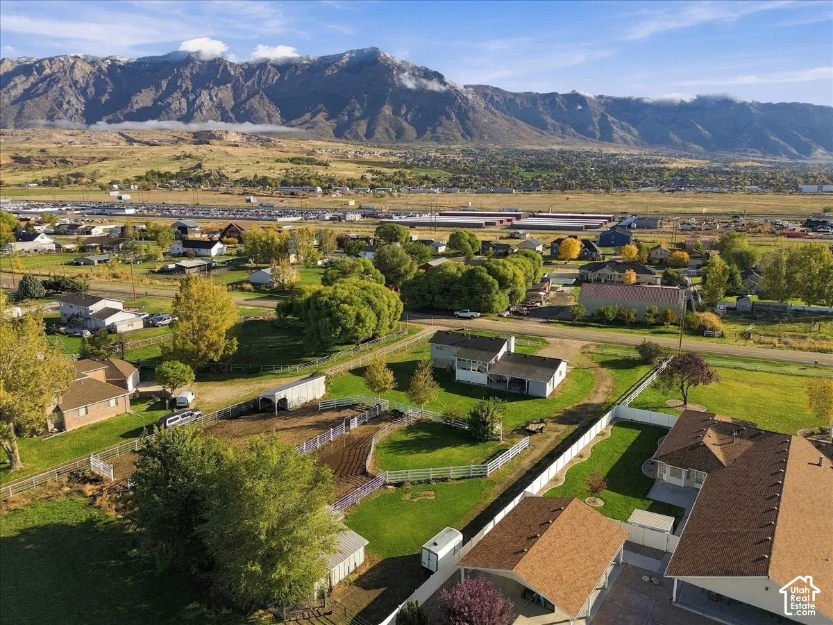 Aerial perspective of the rear of the property featuring expansive acreage, fenced pastures, mature trees, and a mountain backdrop